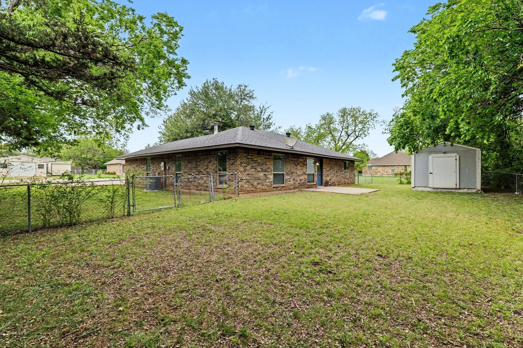 Fenced backyard with lawn, mature trees, and storage shed