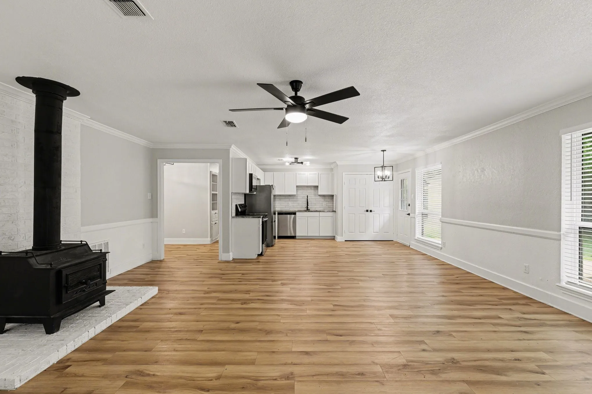 Open living area with plank flooring, ceiling fan, and wood-burning stove
