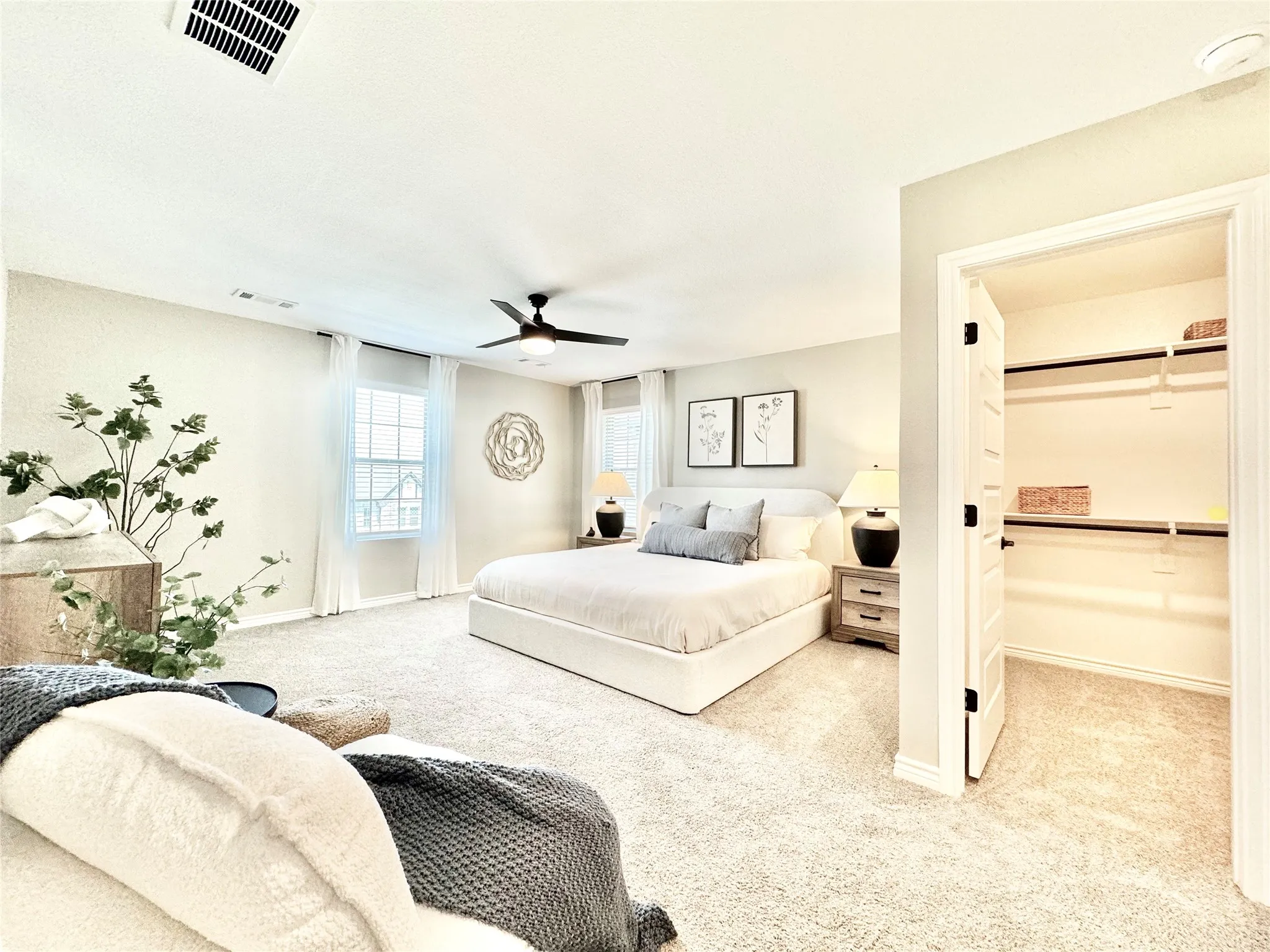 Carpeted bedroom with baseboards, visible vents, a ceiling fan, and a walk in closet
