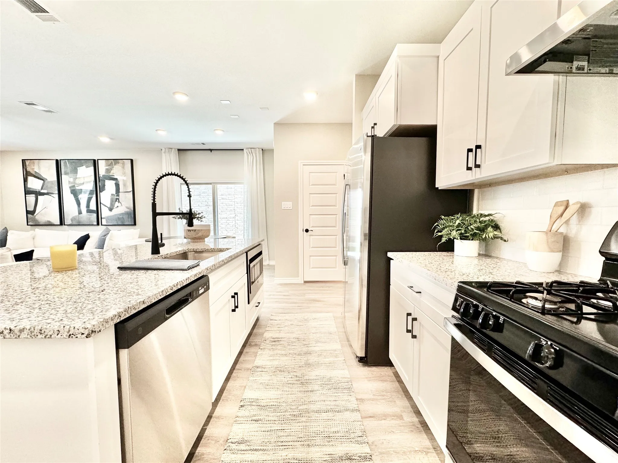 Kitchen with appliances with stainless steel finishes, visible vents, a sink, ventilation hood, and light wood-type flooring