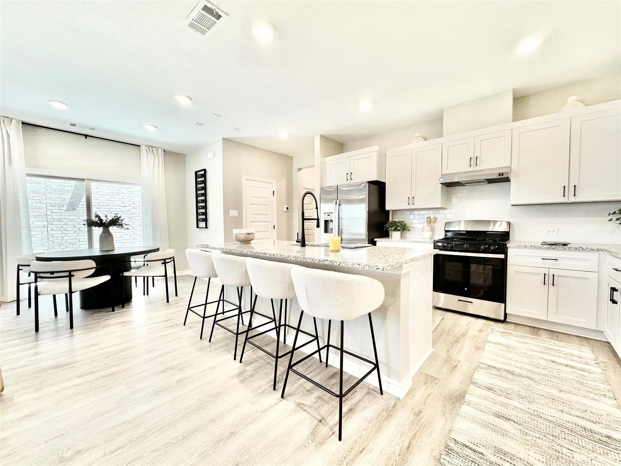 Kitchen with a kitchen island with sink, visible vents, under cabinet range hood, light wood finished floors, and appliances with stainless steel finishes