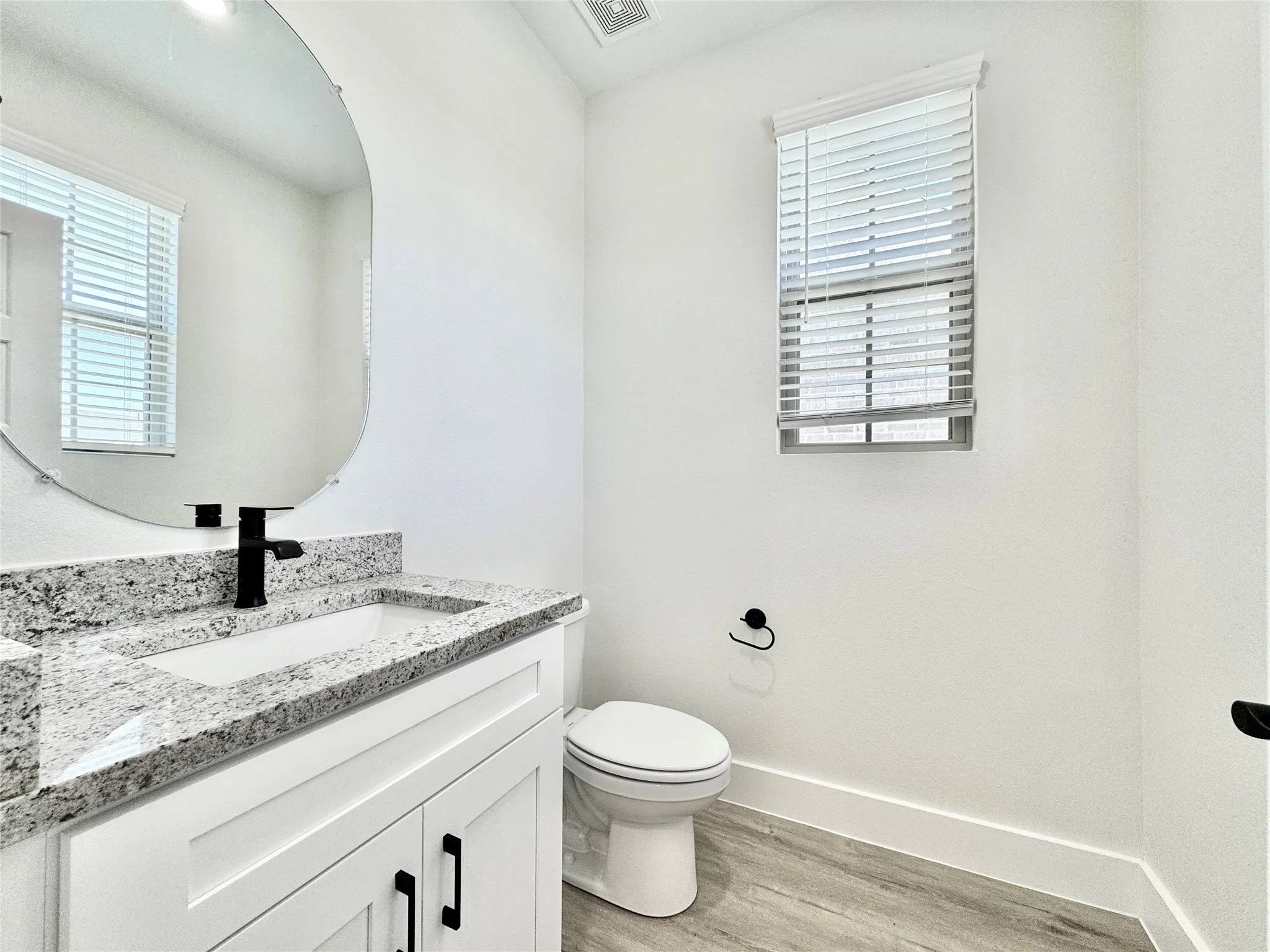 Half bathroom with wood finished floors, baseboards, toilet, vanity, and plenty of natural light