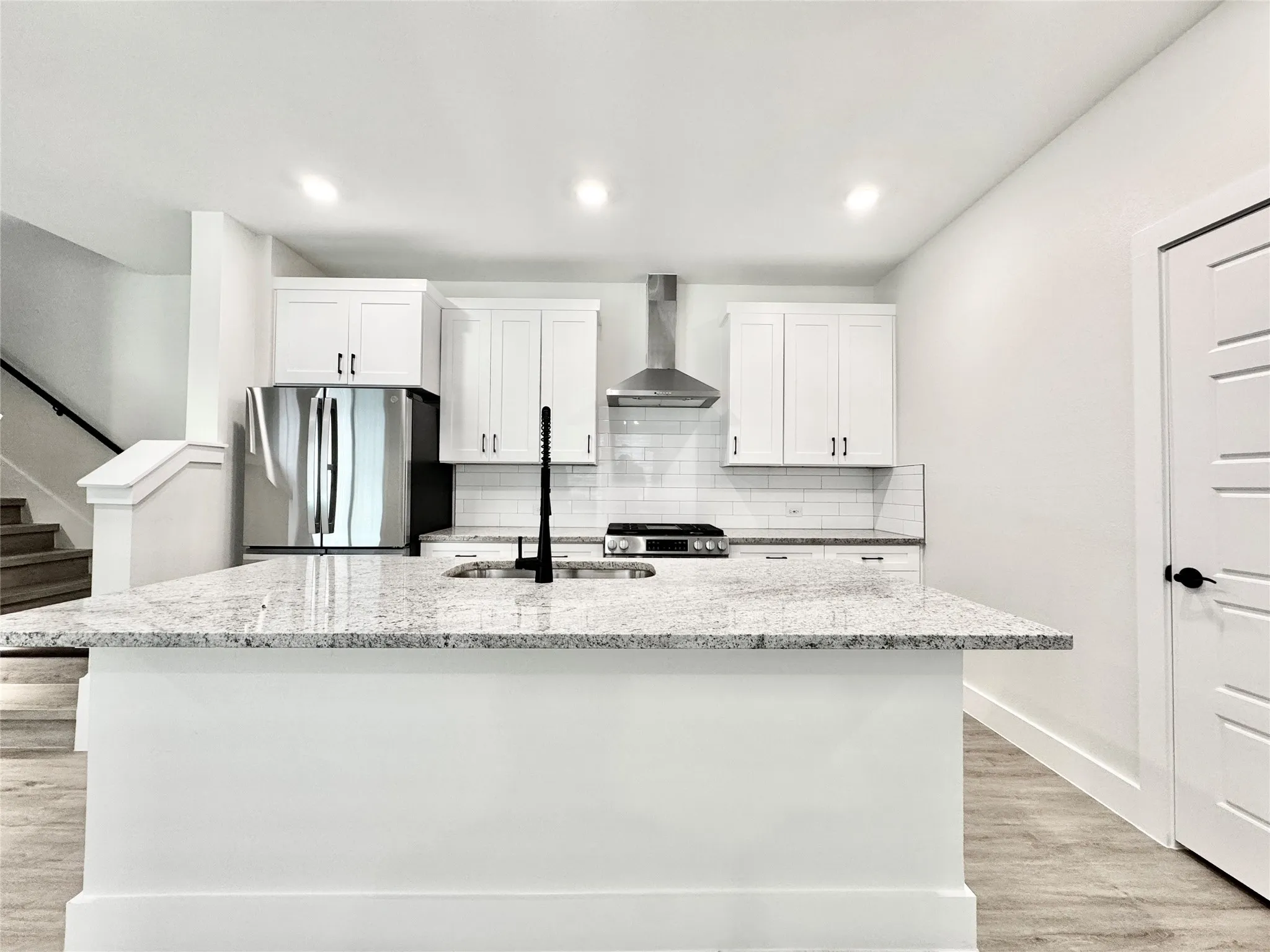 Kitchen featuring stainless steel appliances, wall chimney exhaust hood, a sink, white cabinetry, and a kitchen island with sink