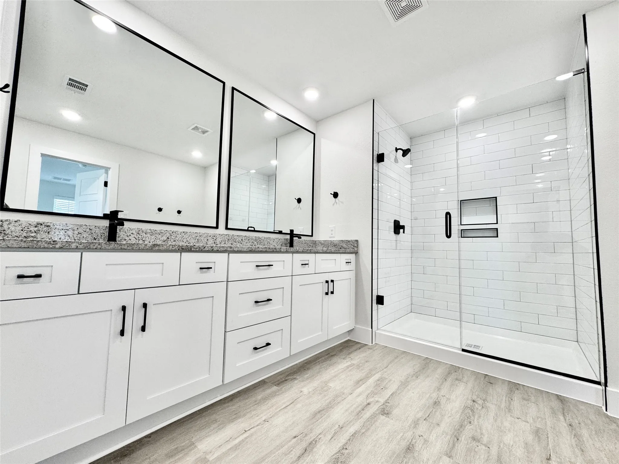 Bathroom with wood finished floors, a shower stall, double vanity, and recessed lighting
