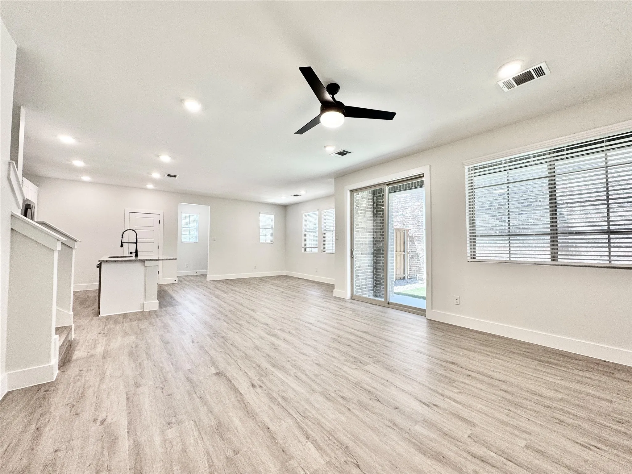 Unfurnished living room featuring a sink, light wood finished floors, ceiling fan, baseboards, and recessed lighting