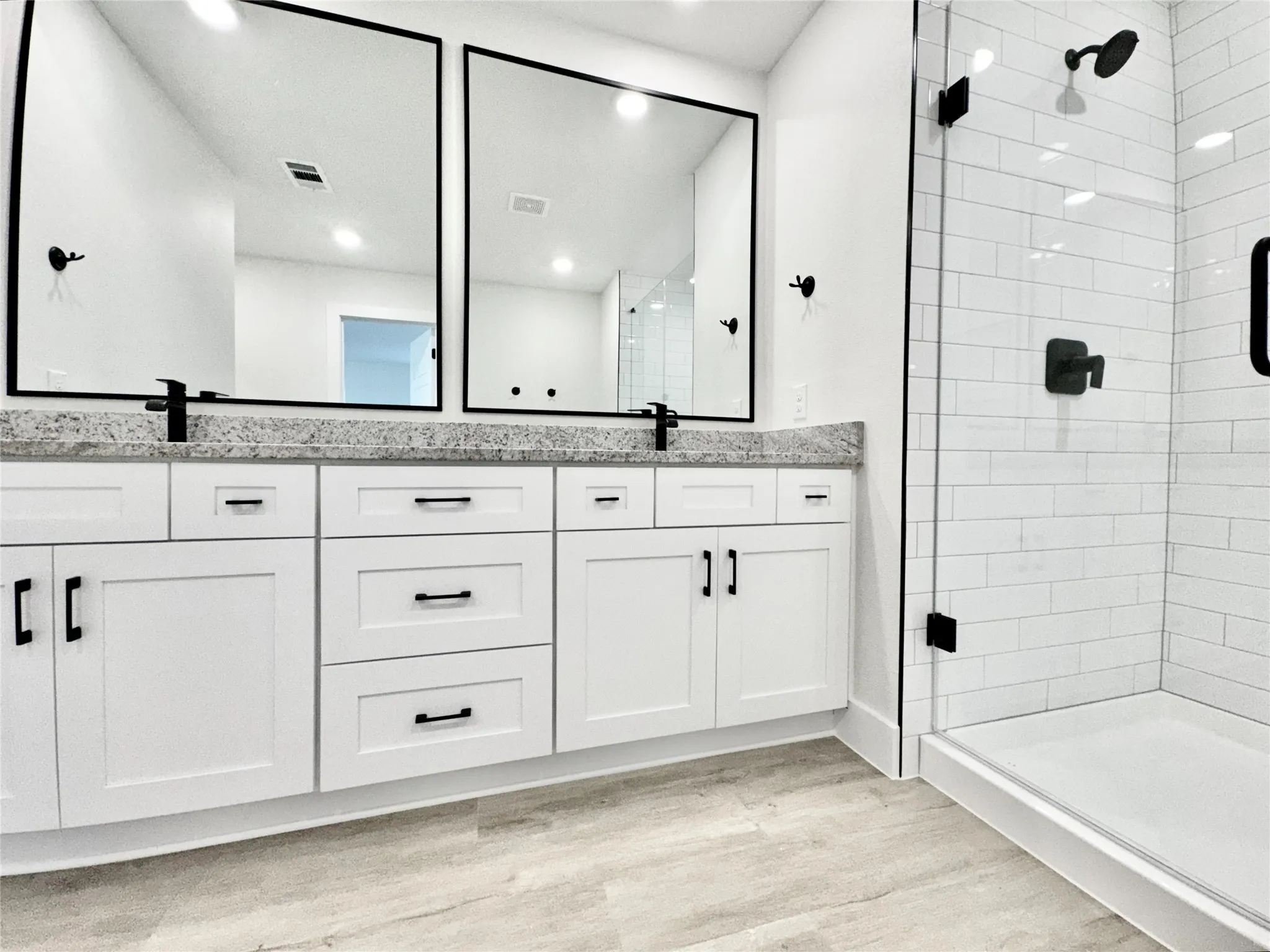 Bathroom featuring wood finished floors, a stall shower, double vanity, and recessed lighting