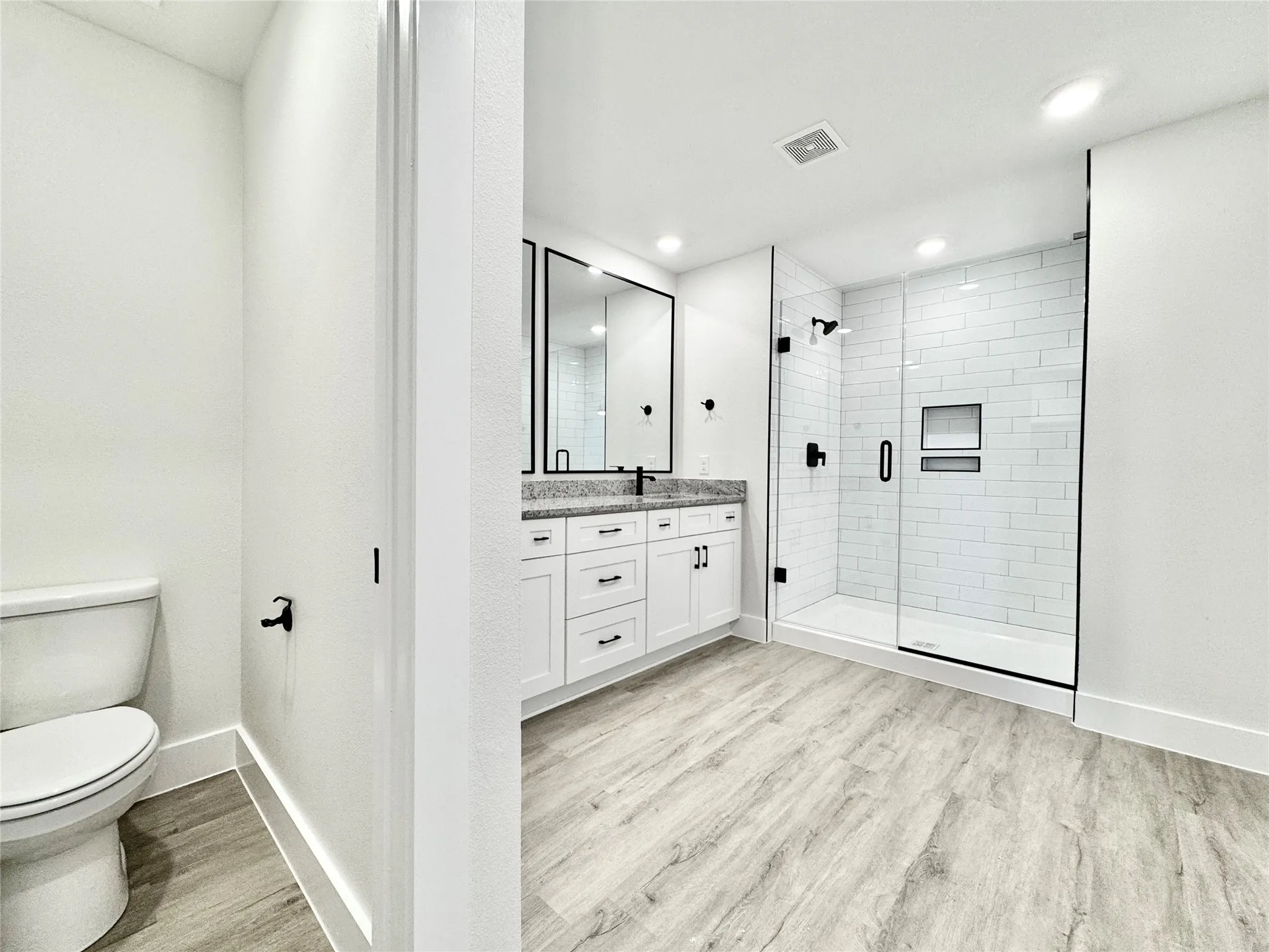 Full bath featuring toilet, wood finished floors, a stall shower, baseboards, and vanity