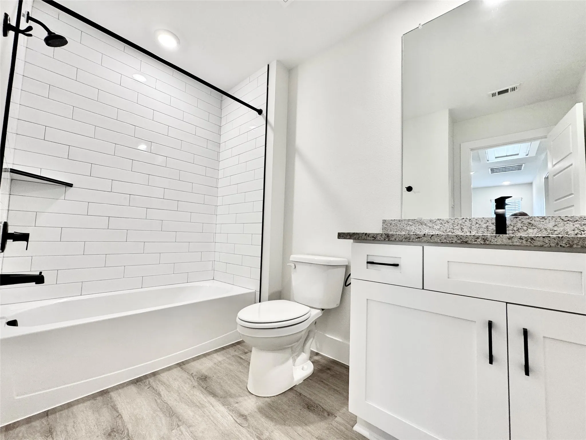 Full bathroom with wood finished floors, toilet, shower / washtub combination, vanity, and baseboards