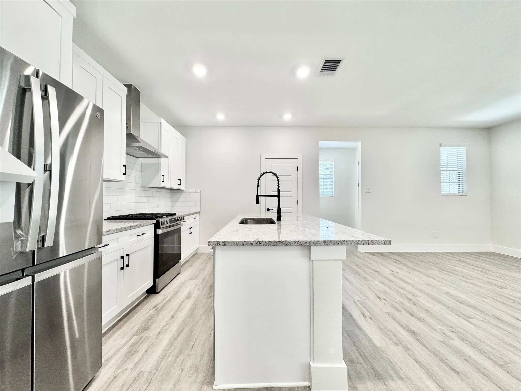 Kitchen with appliances with stainless steel finishes, a sink, wall chimney range hood, light wood-style flooring, and an island with sink