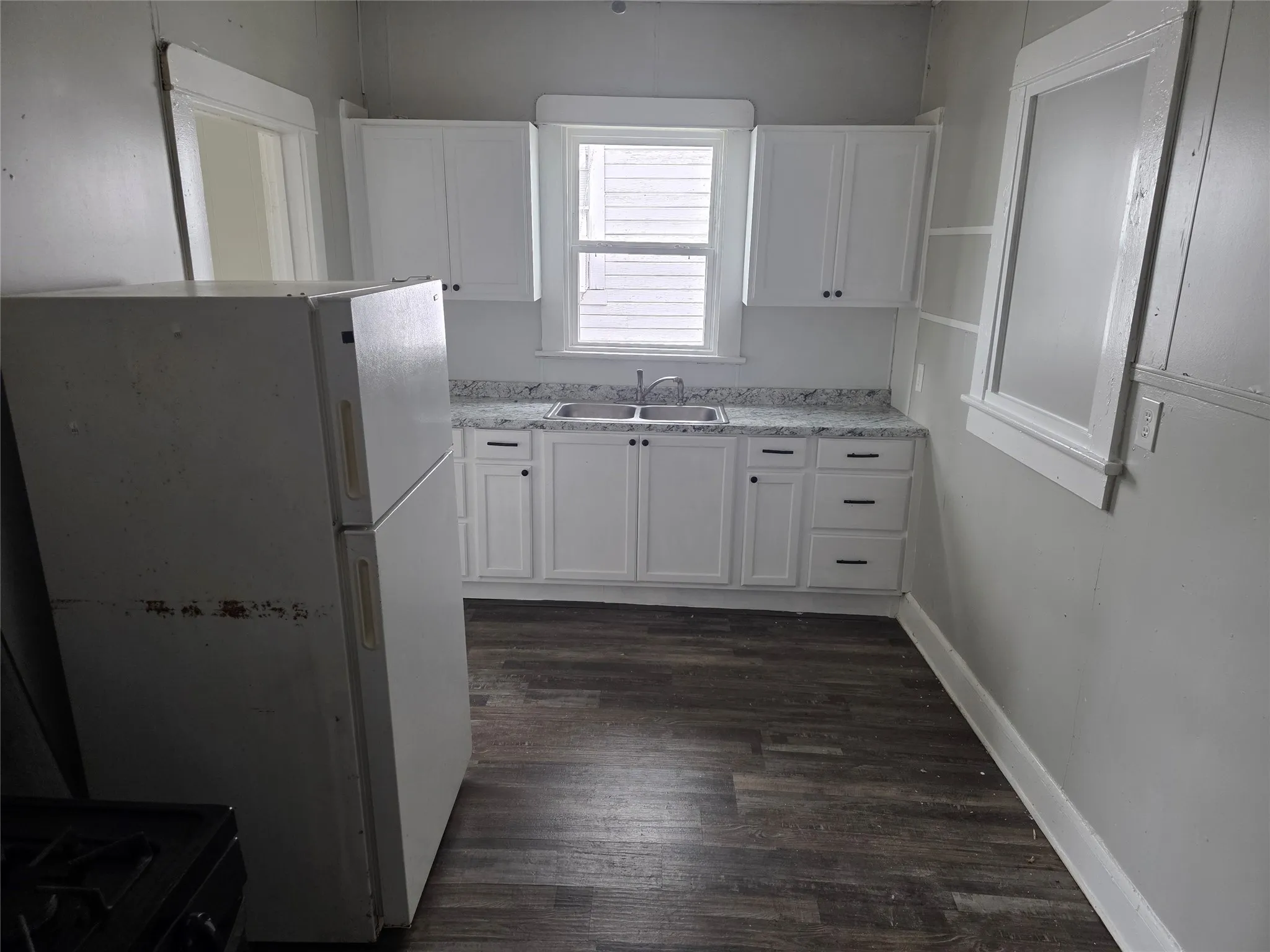 The kitchen features white cabinetry with dark hardware, a double basin sink, and wood-look flooring