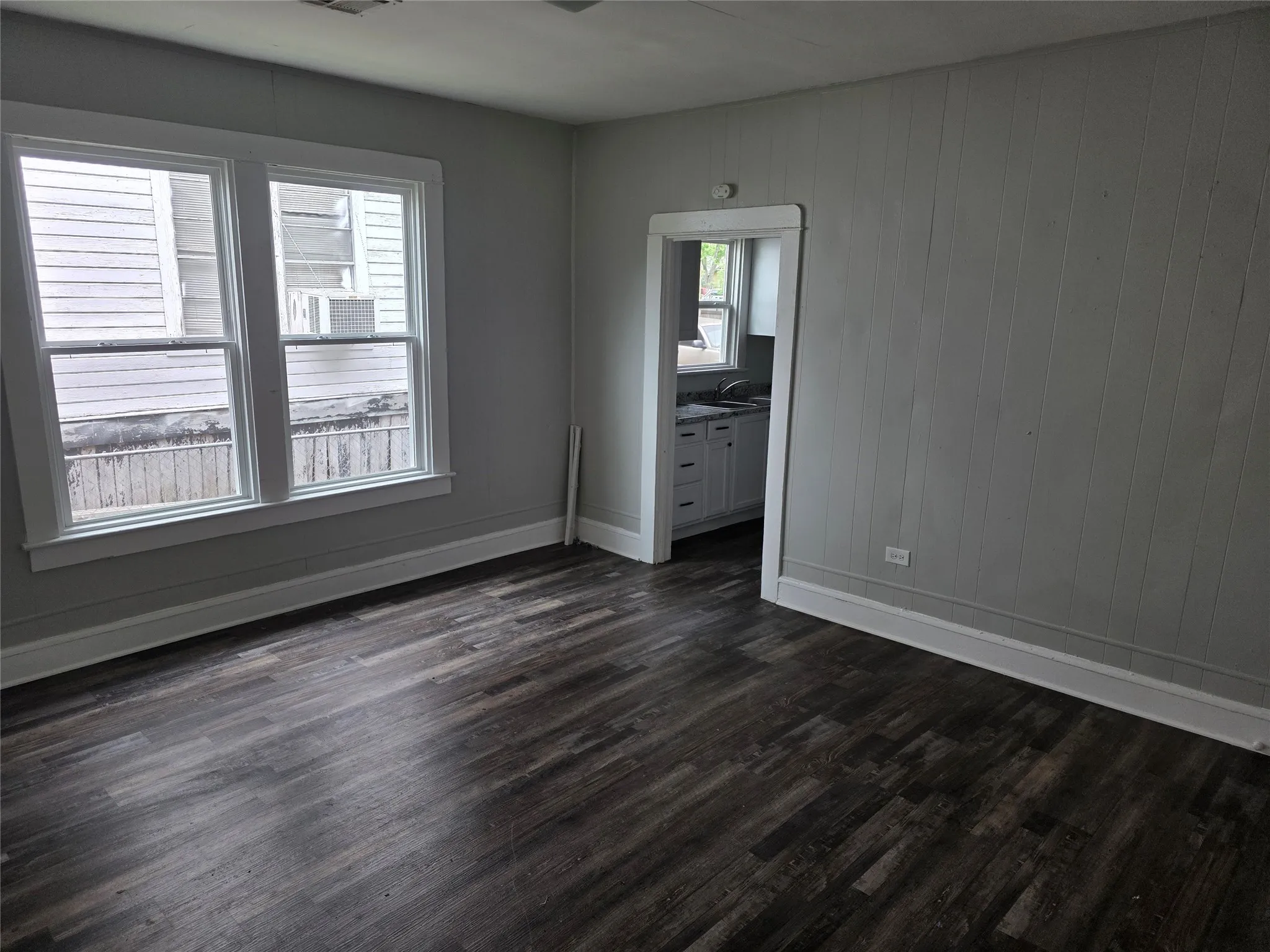 Living area featuring dark wood-style flooring, light-toned walls, and two windows with white trim