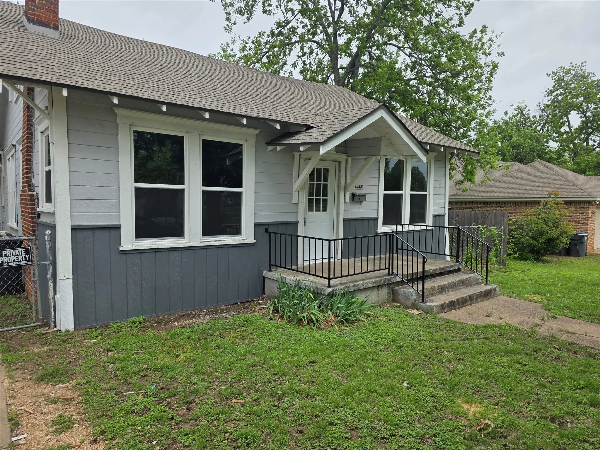 The property features a concrete porch with black metal railings, a light-colored front door