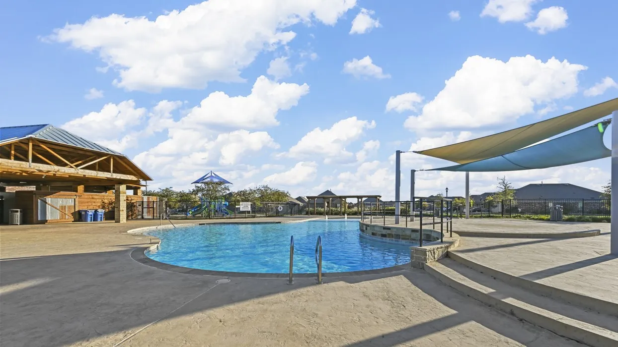 The property offers access to a community pool with a surrounding paved deck, a shaded lounging area, and a nearby open-air structure