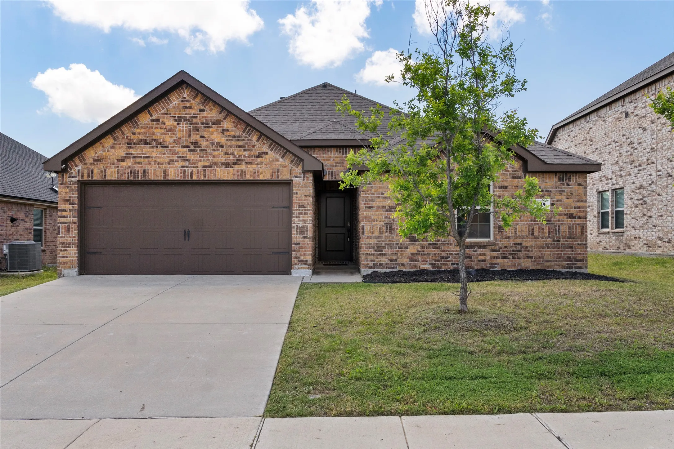 The property features a brick exterior, an attached garage, a driveway, and a front yard with a tree