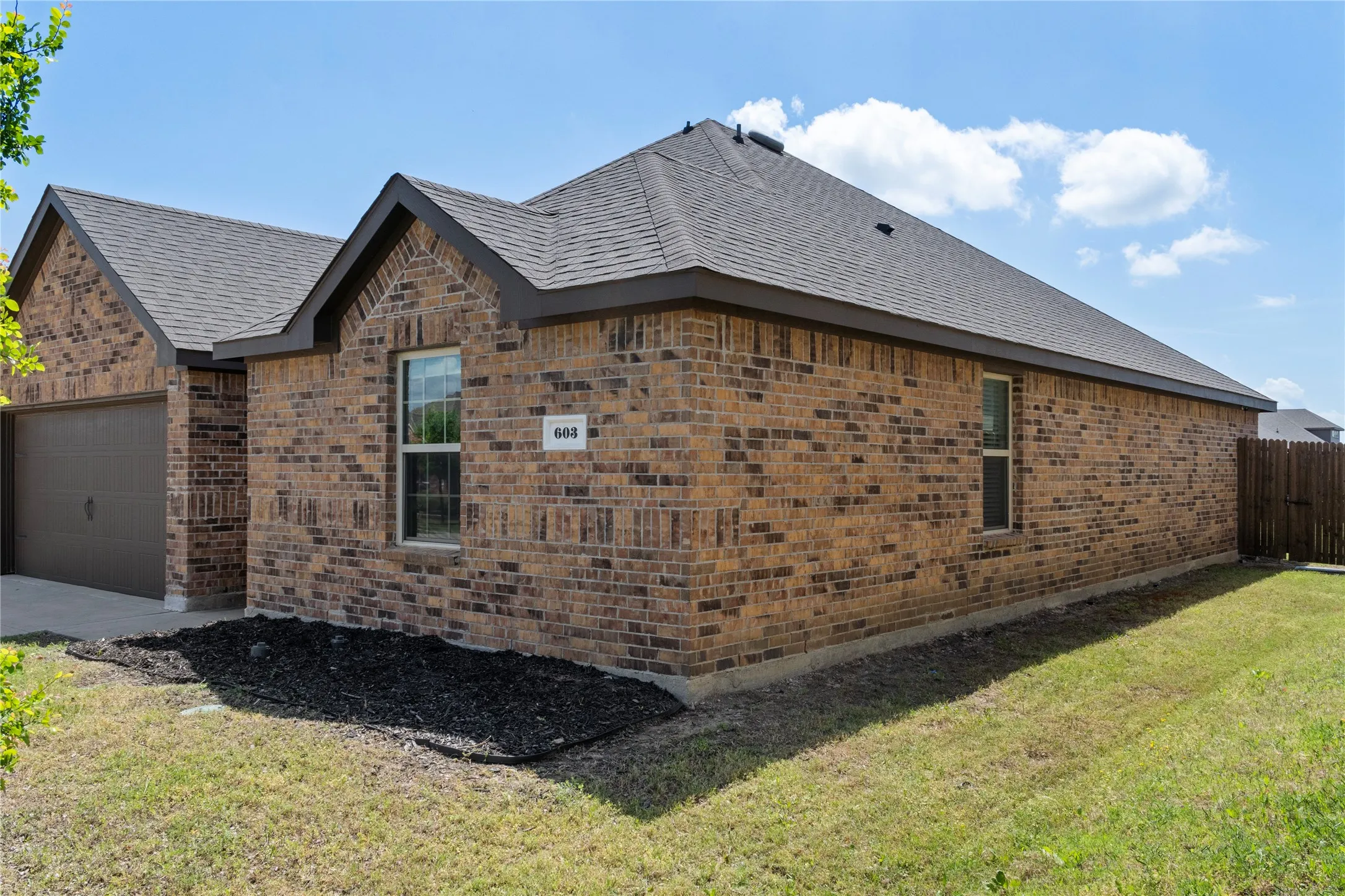 The property features a brick exterior, an attached garage, a dark shingle roof, and a neatly maintained lawn