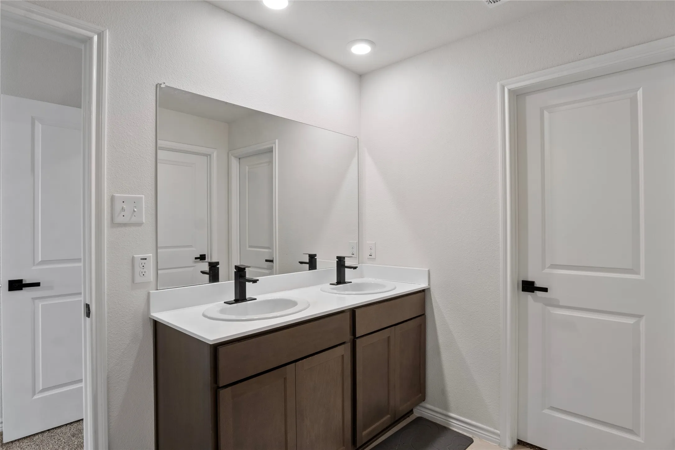 This bathroom features a double vanity with dark wood cabinetry, white countertops, and dual sinks with matte black faucets
