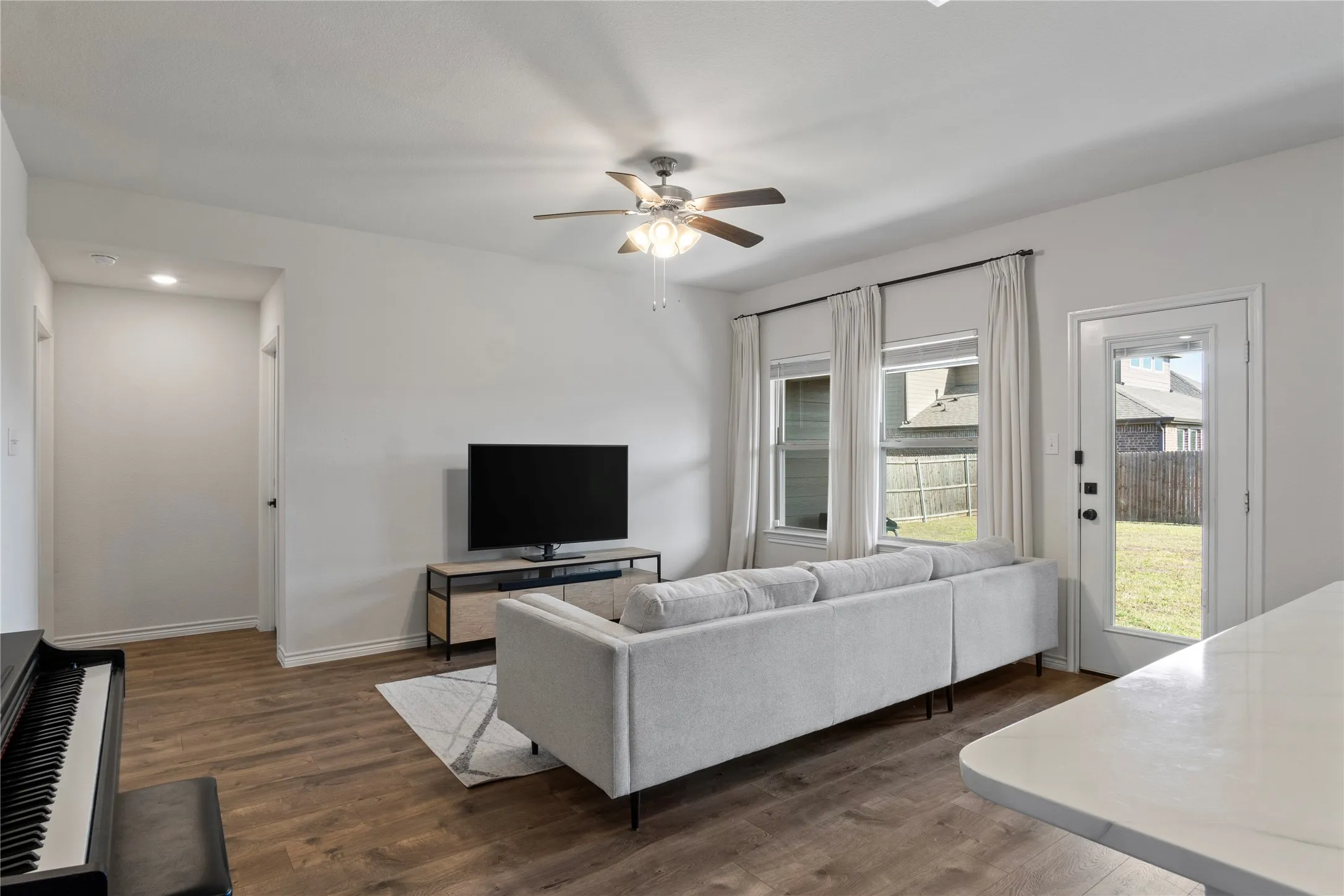 Spacious living area featuring durable flooring, a ceiling fan, and access to the outdoors through a glass paneled door