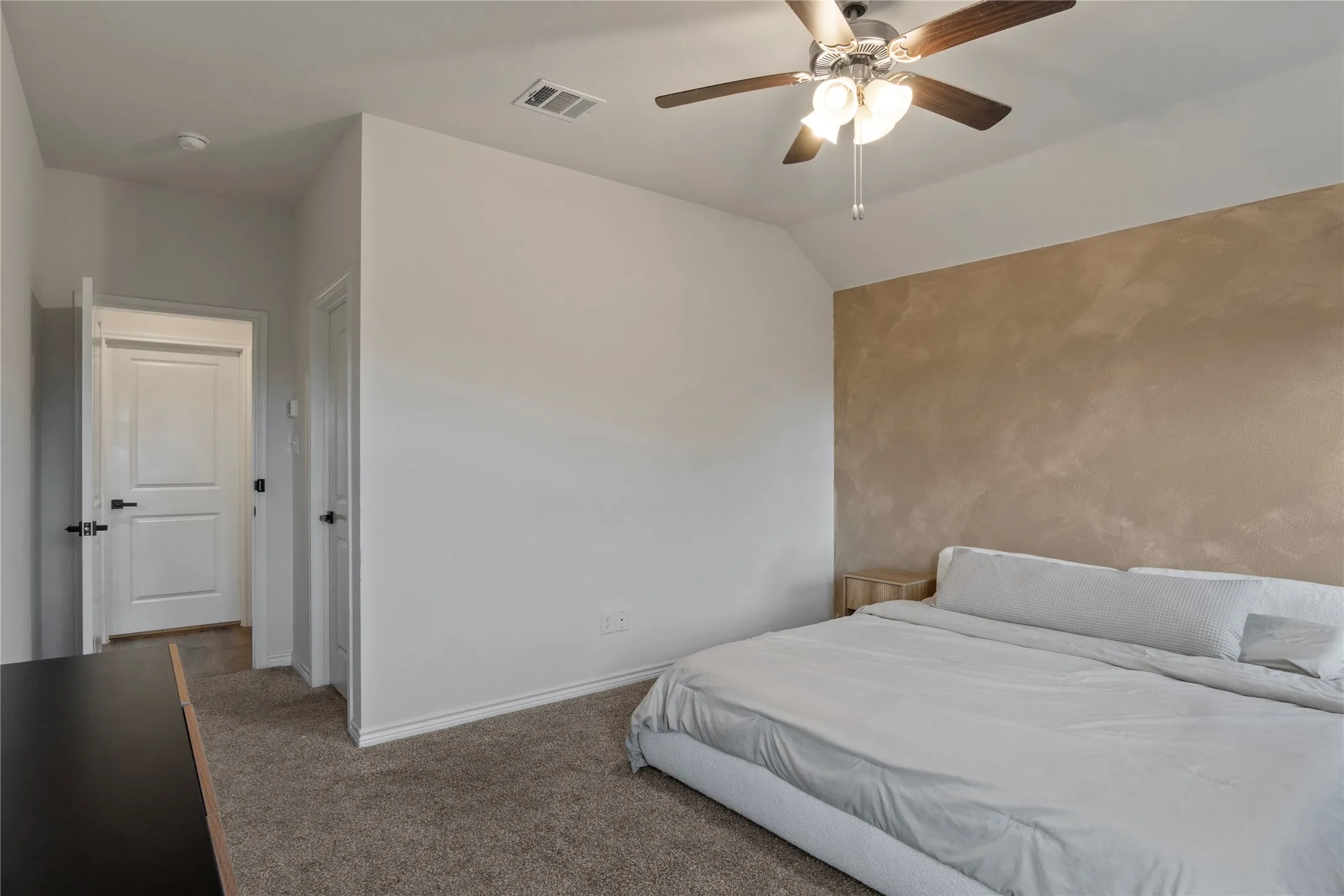 This spacious room features a textured accent wall, soft carpeting, and a ceiling fan with integrated lighting