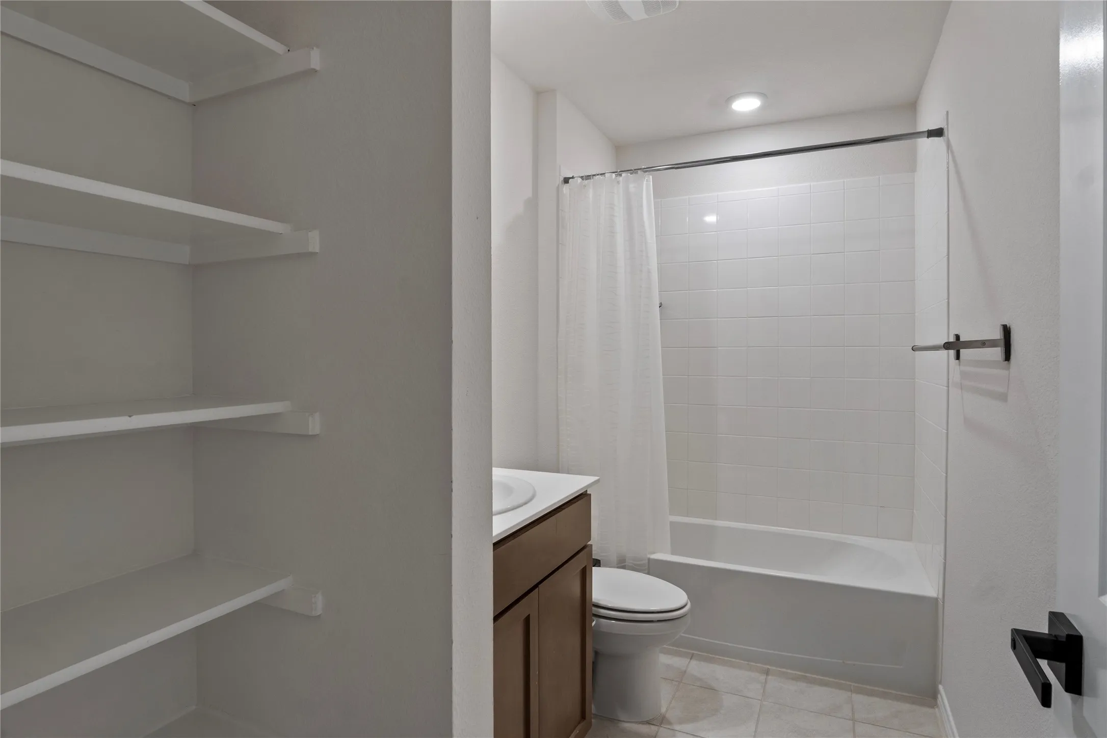 Bathroom featuring white tiled walls in the shower area, a white bathtub, and a wooden vanity with a white countertop and a sink