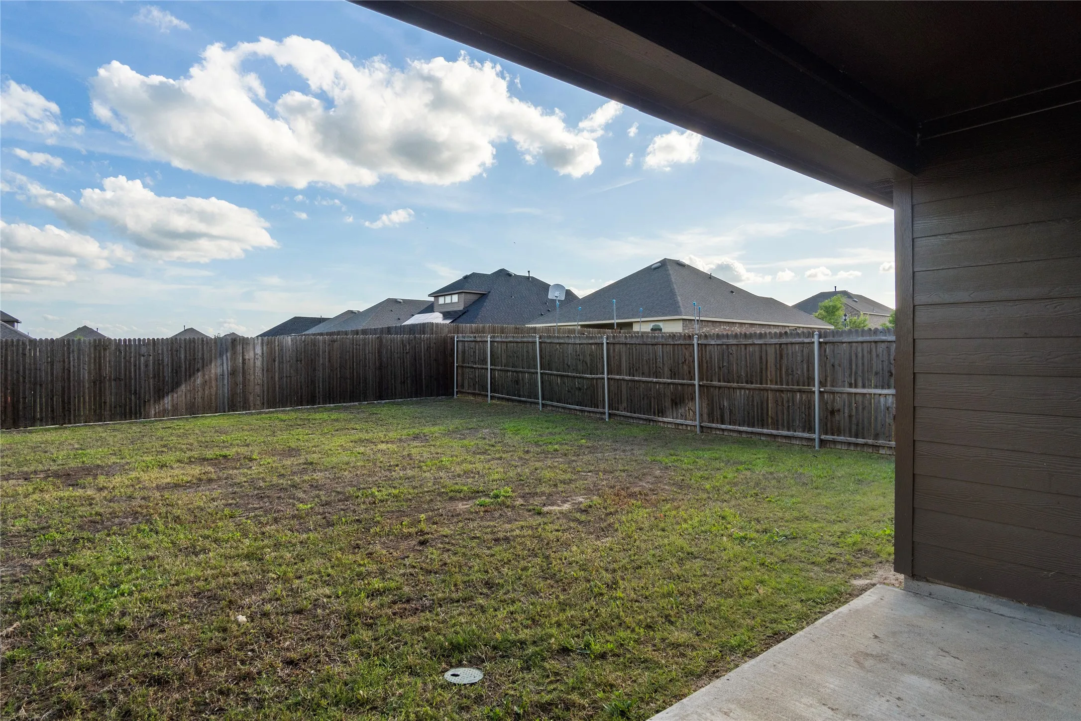 The property features an expansive yard with a wooden fence and a concrete patio area, providing a versatile outdoor space