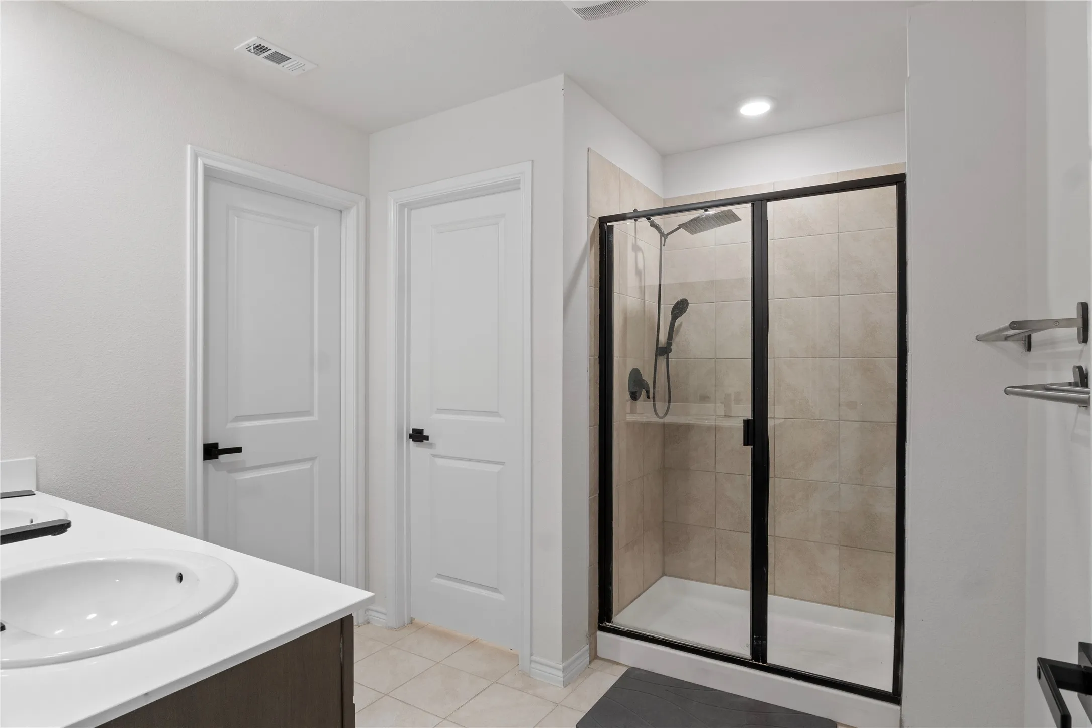 Bathroom featuring a vanity with a white countertop and an undermount sink, two white panel doors with dark hardware, and a walk-in shower with a black-framed glass enclosure and tiled walls