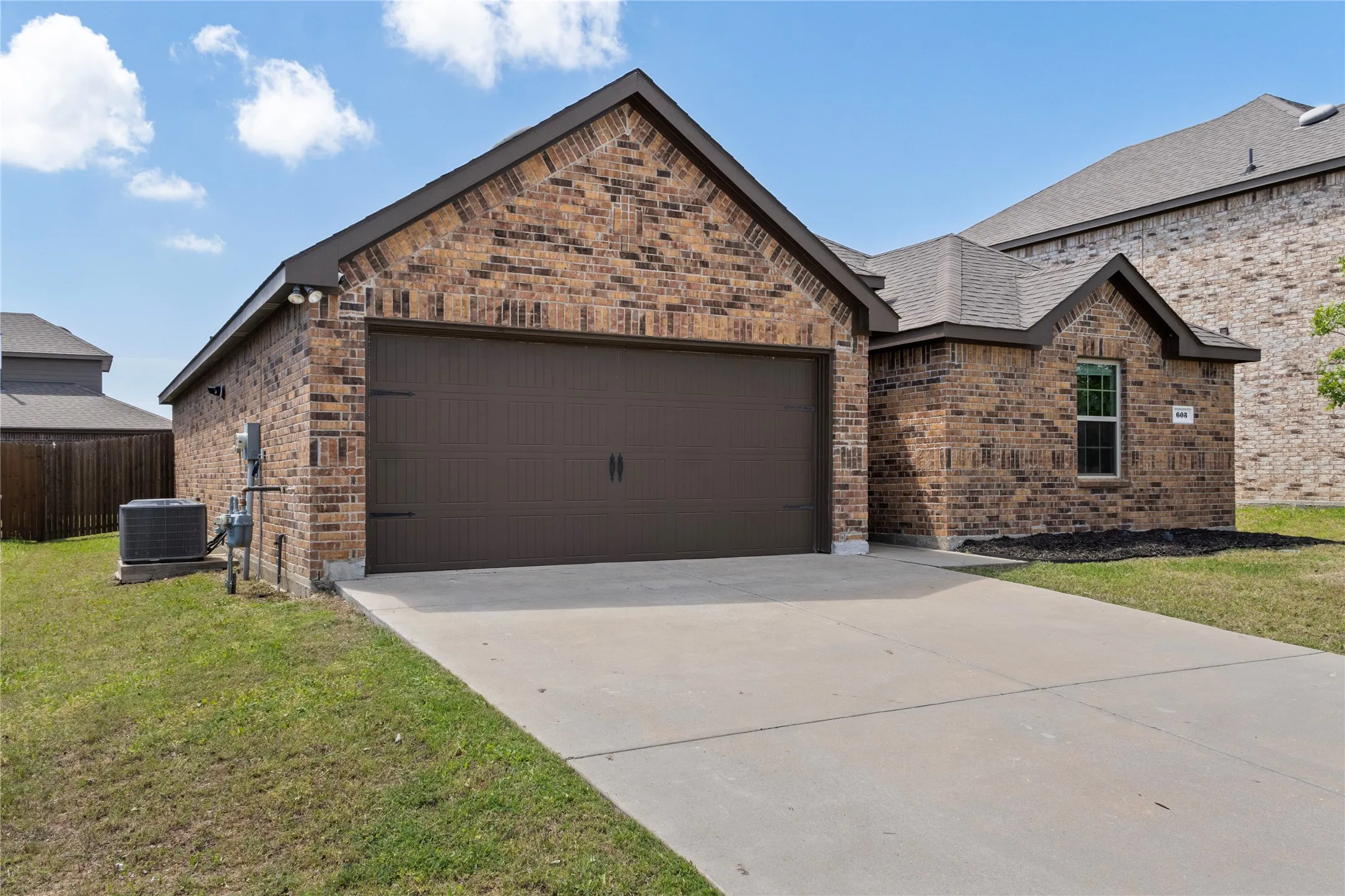 The property features an exterior of brick, a brown garage door, and a concrete driveway