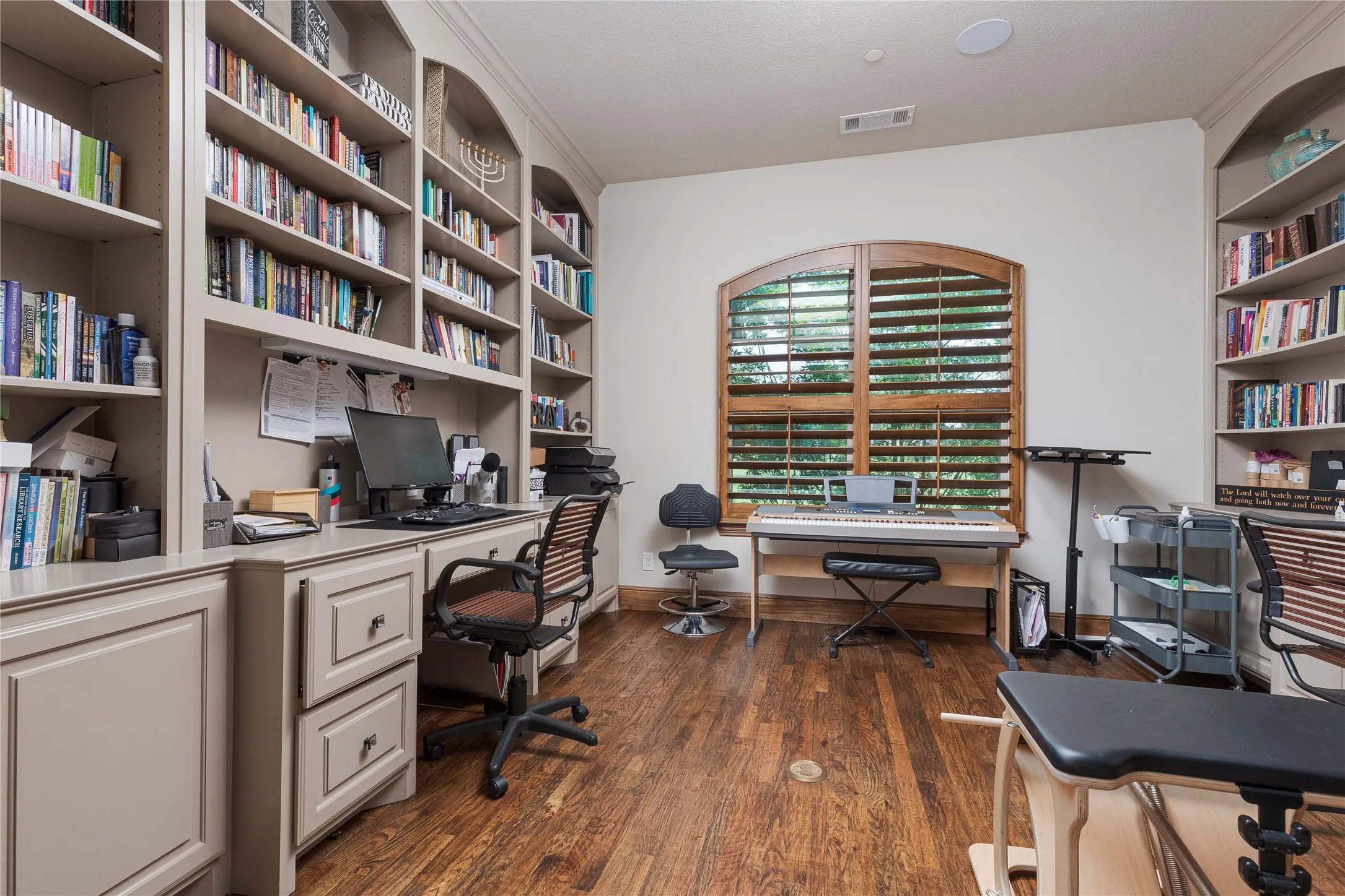 Home office featuring dark wood-type flooring, visible vents, built in shelves, and baseboards