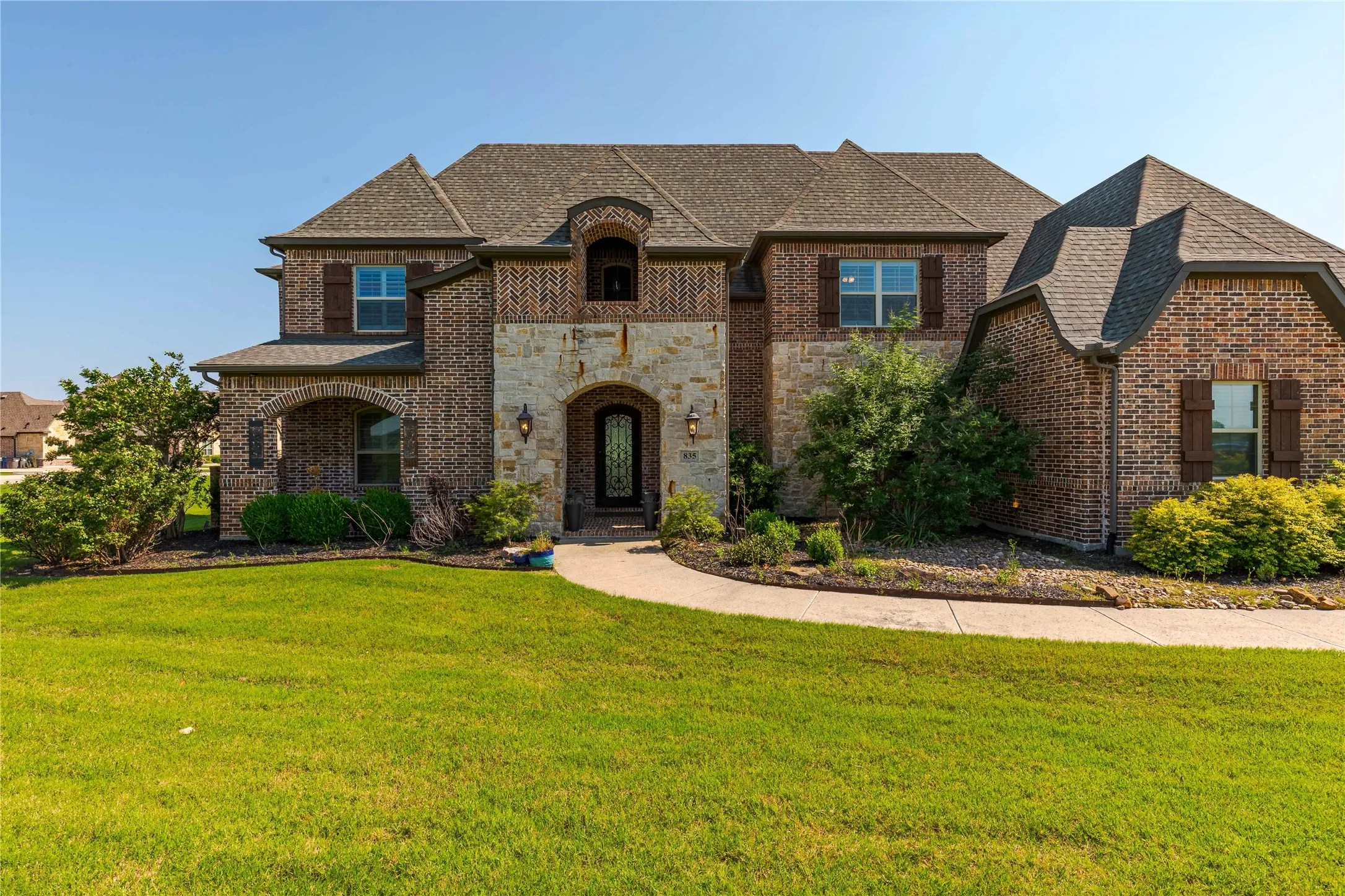 French country style house with stone siding, a shingled roof, brick siding, and a front yard