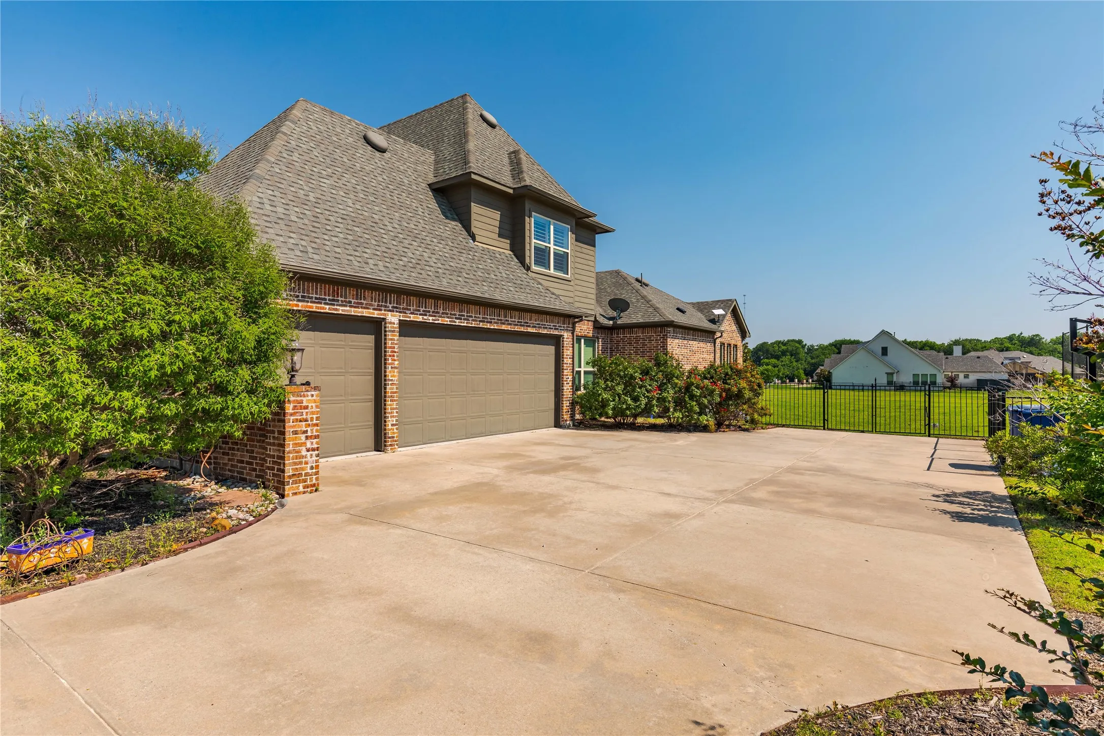 View of home's exterior featuring roof with shingles, driveway, fence, brick siding, and a garage