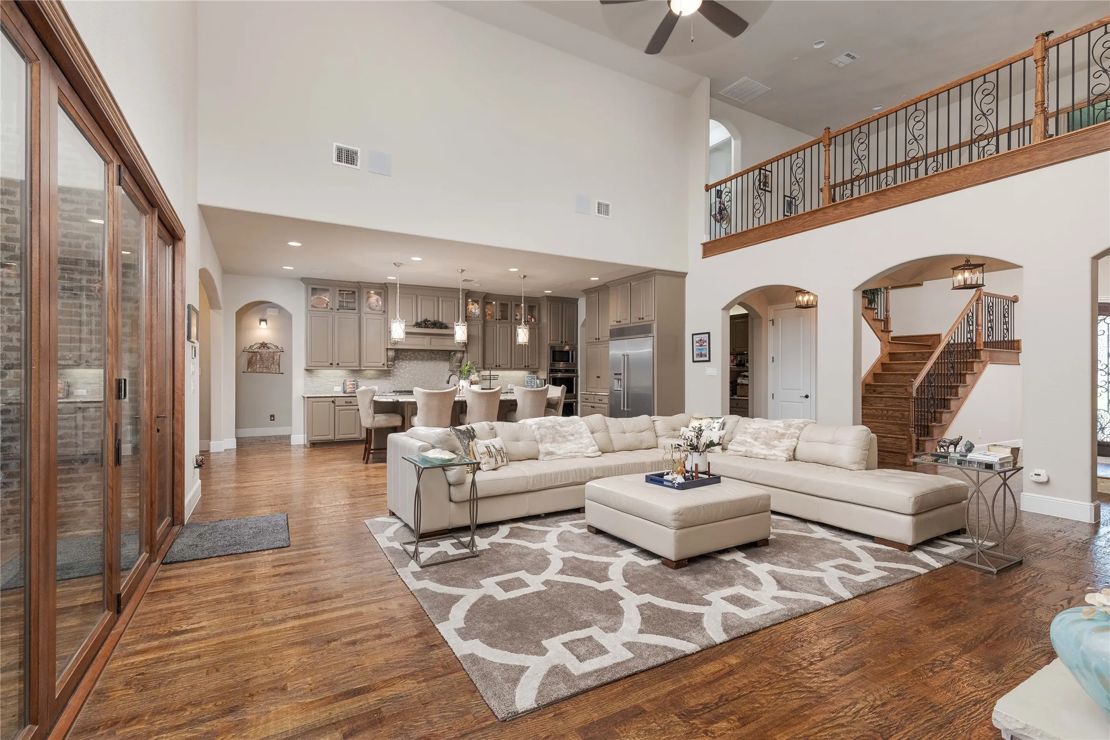 Living room featuring arched walkways, a towering ceiling, wood finished floors, stairs, and ceiling fan