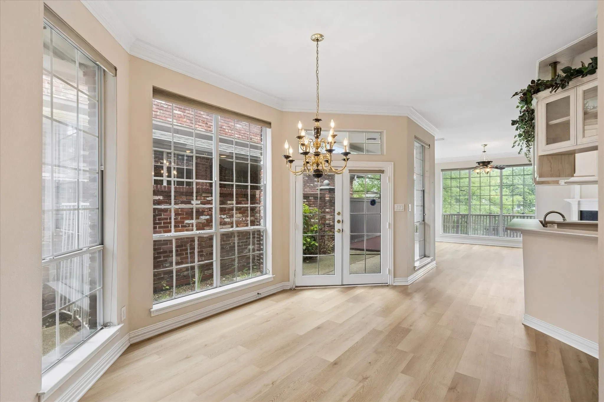 This bright living space features light-toned flooring, large windows with white grids, and a double-door entry leading to an exterior area