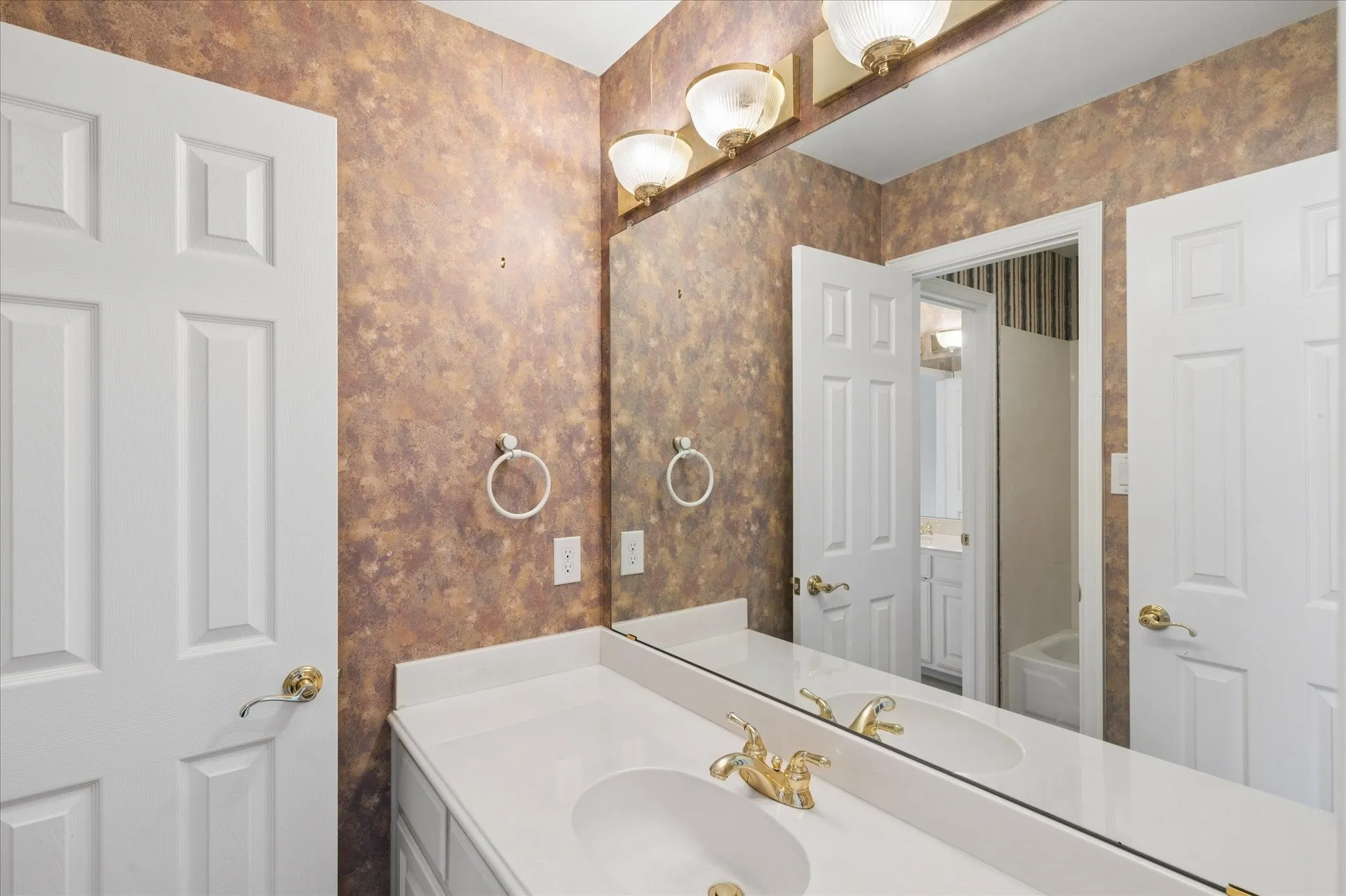 Bathroom featuring a vanity with a white countertop and an integrated sink, illuminated by a three-light fixture above a large mirror