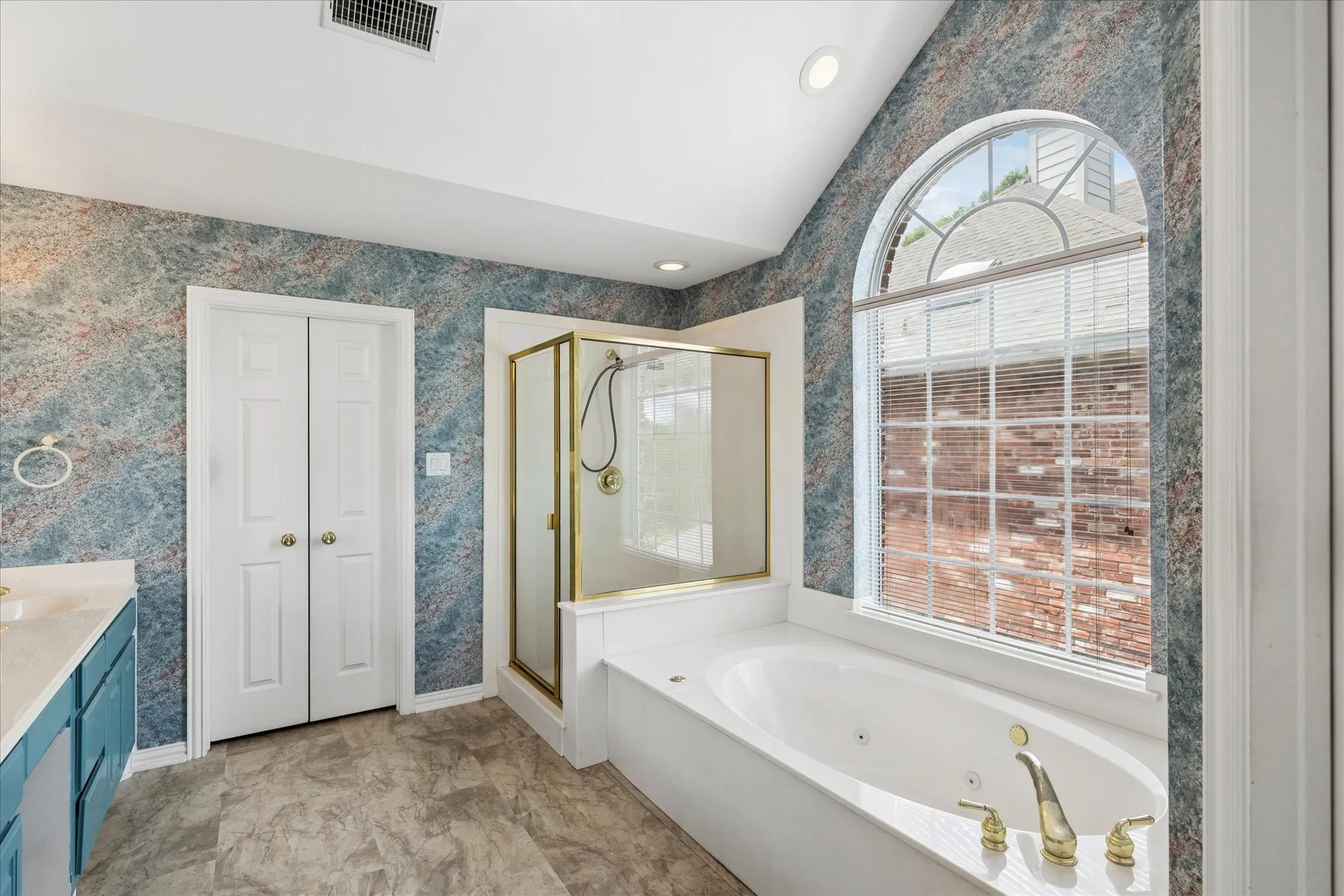 Bathroom featuring a large arched window, a built-in bathtub with gold-toned fixtures, a glass-enclosed shower, and a vanity with a white countertop