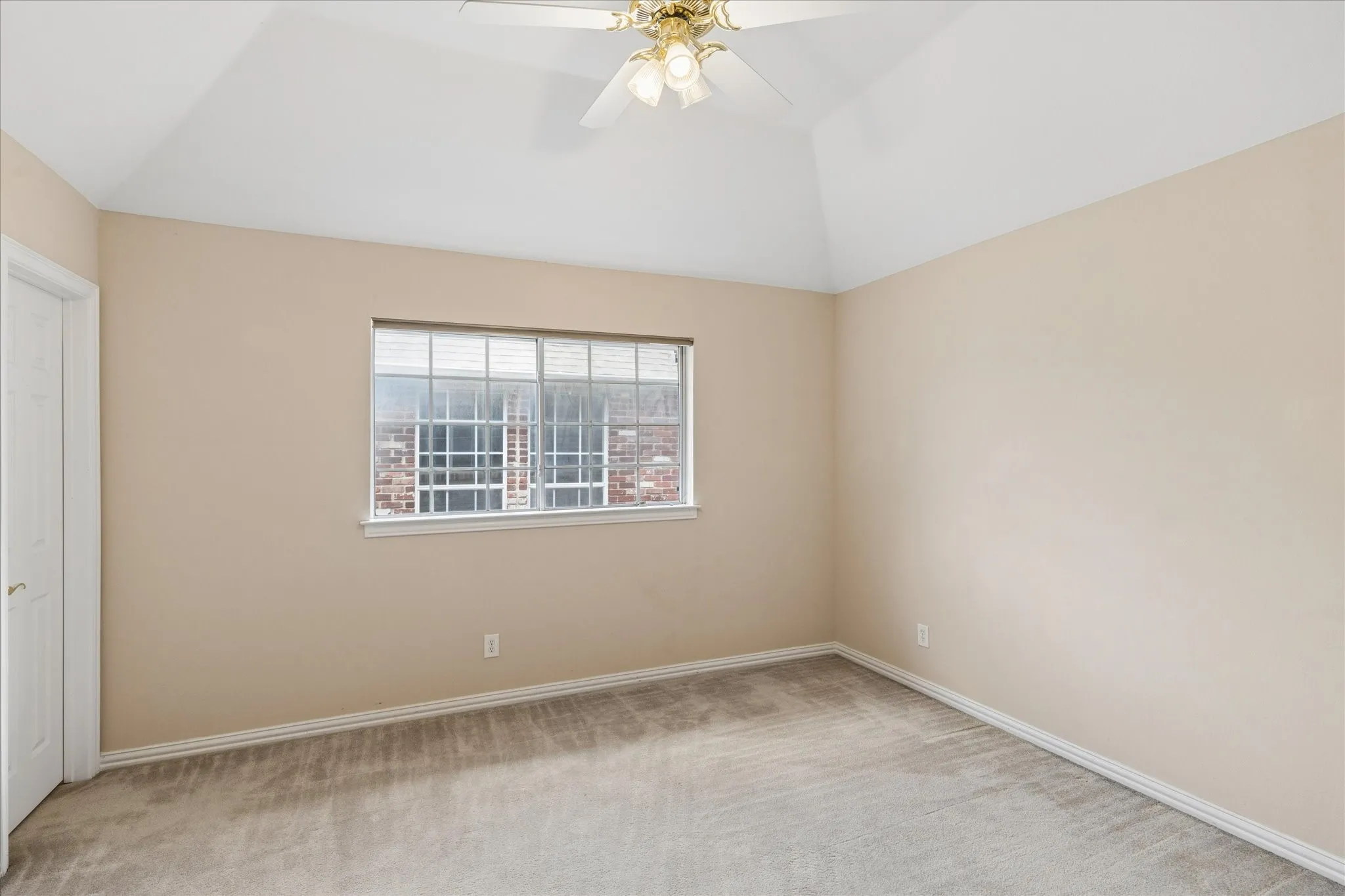 This room features a vaulted ceiling with a ceiling fan, carpeted flooring, and a window with blinds