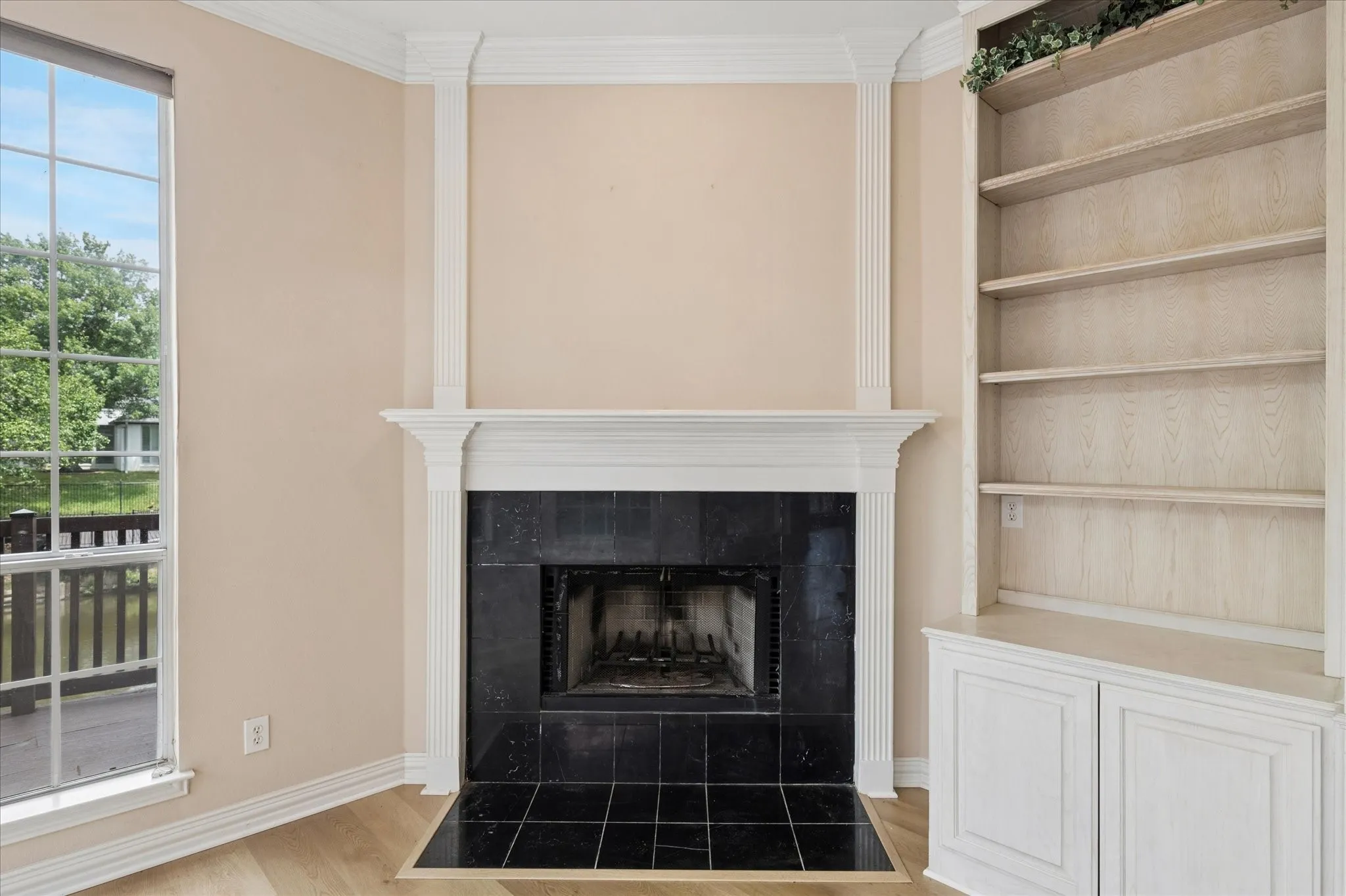 Living area featuring a fireplace with a black tile surround, a built-in bookshelf with cabinet storage, and a large window overlooking lush greenery