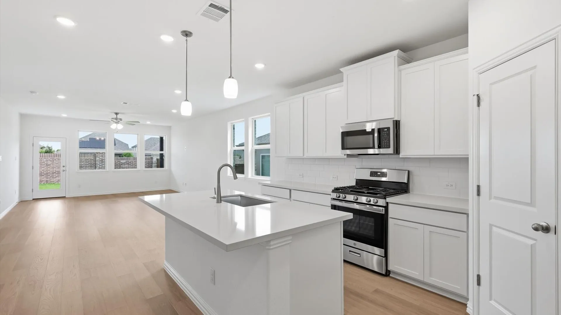 Modern kitchen featuring an island with an undermount sink, pendant lighting, stainless steel appliances, white cabinetry, and wood-finish flooring