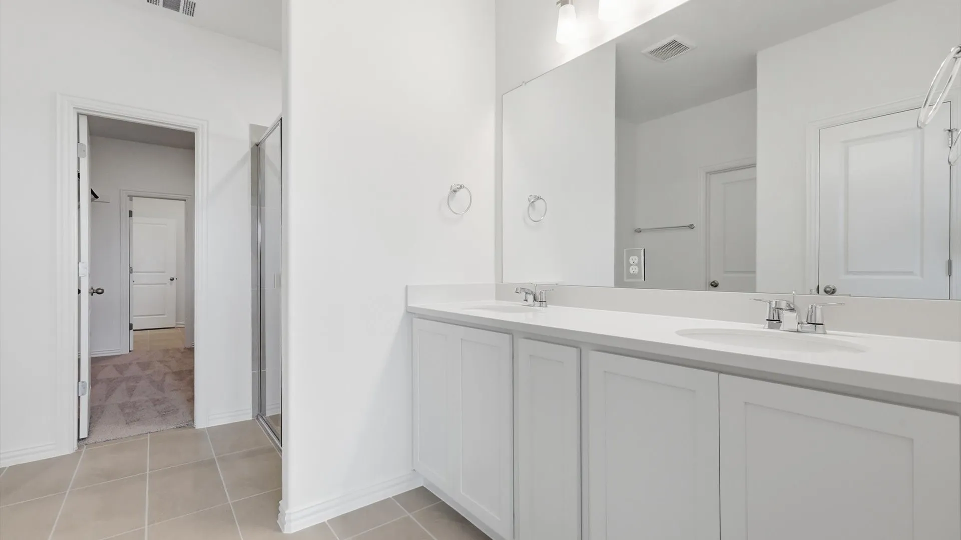 Dual vanity with undermount sinks and chrome fixtures, ample countertop space, large wall-mounted mirror, and tile flooring
