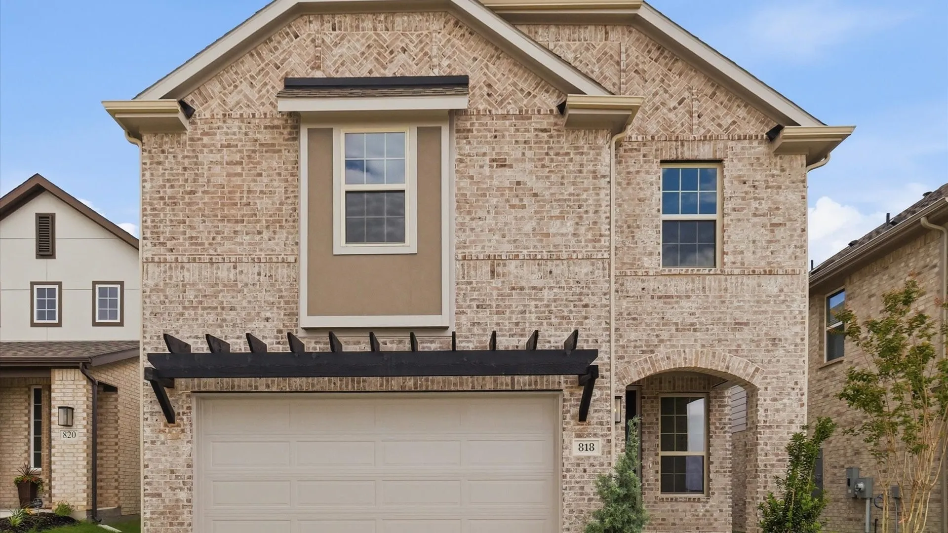 Two-story brick exterior featuring a multi-pane window, arched entry, black decorative pergola, and an attached garage