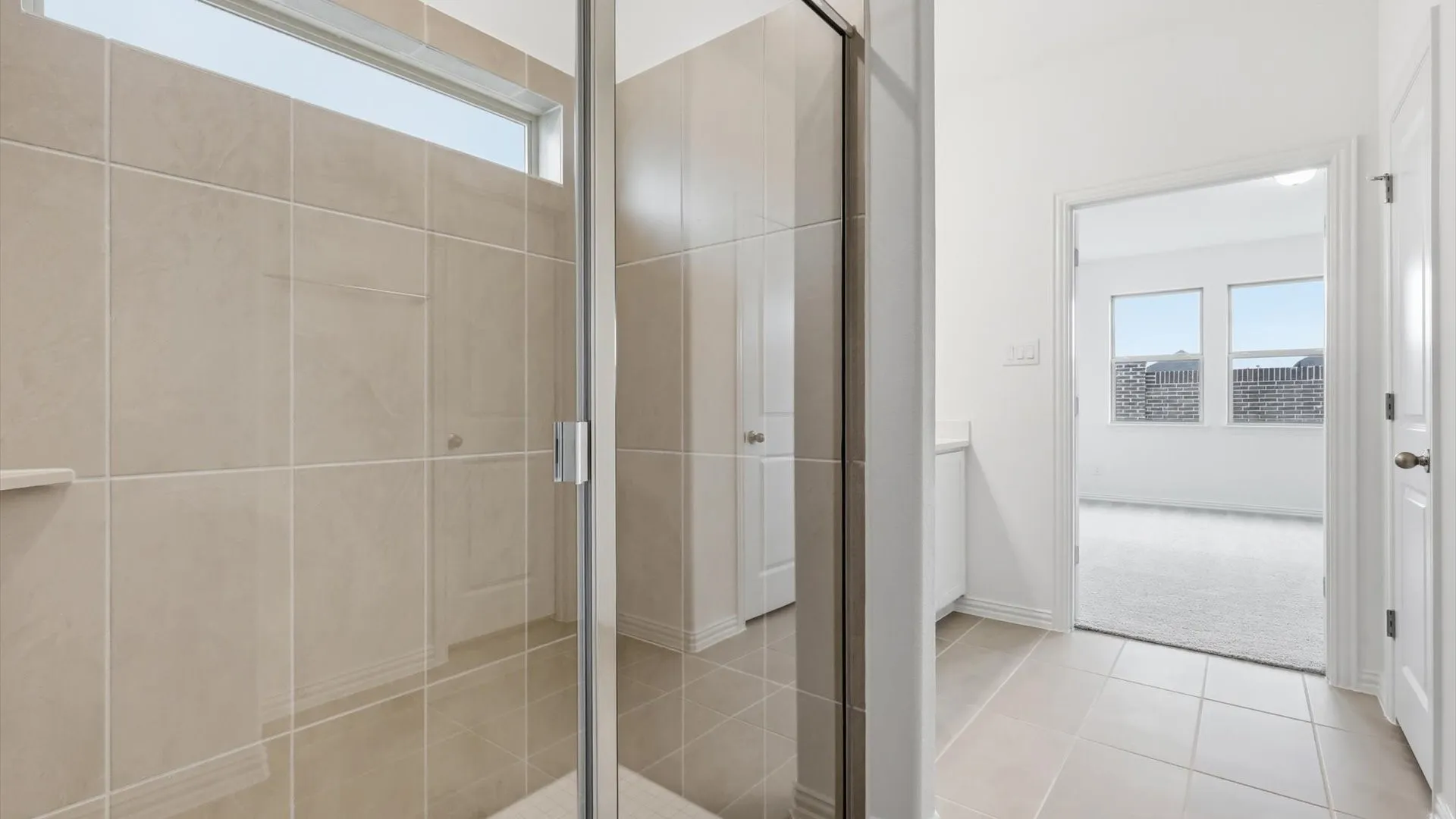 Spacious shower with glass enclosure, light-toned tile surround, and an integrated shelf