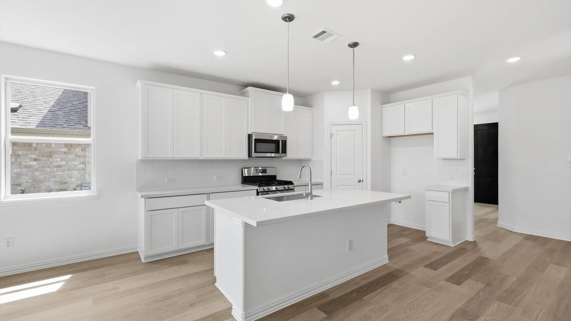 Kitchen featuring an island with a stainless steel sink and gooseneck faucet, white shaker cabinetry, stainless steel microwave, and wood-finish flooring