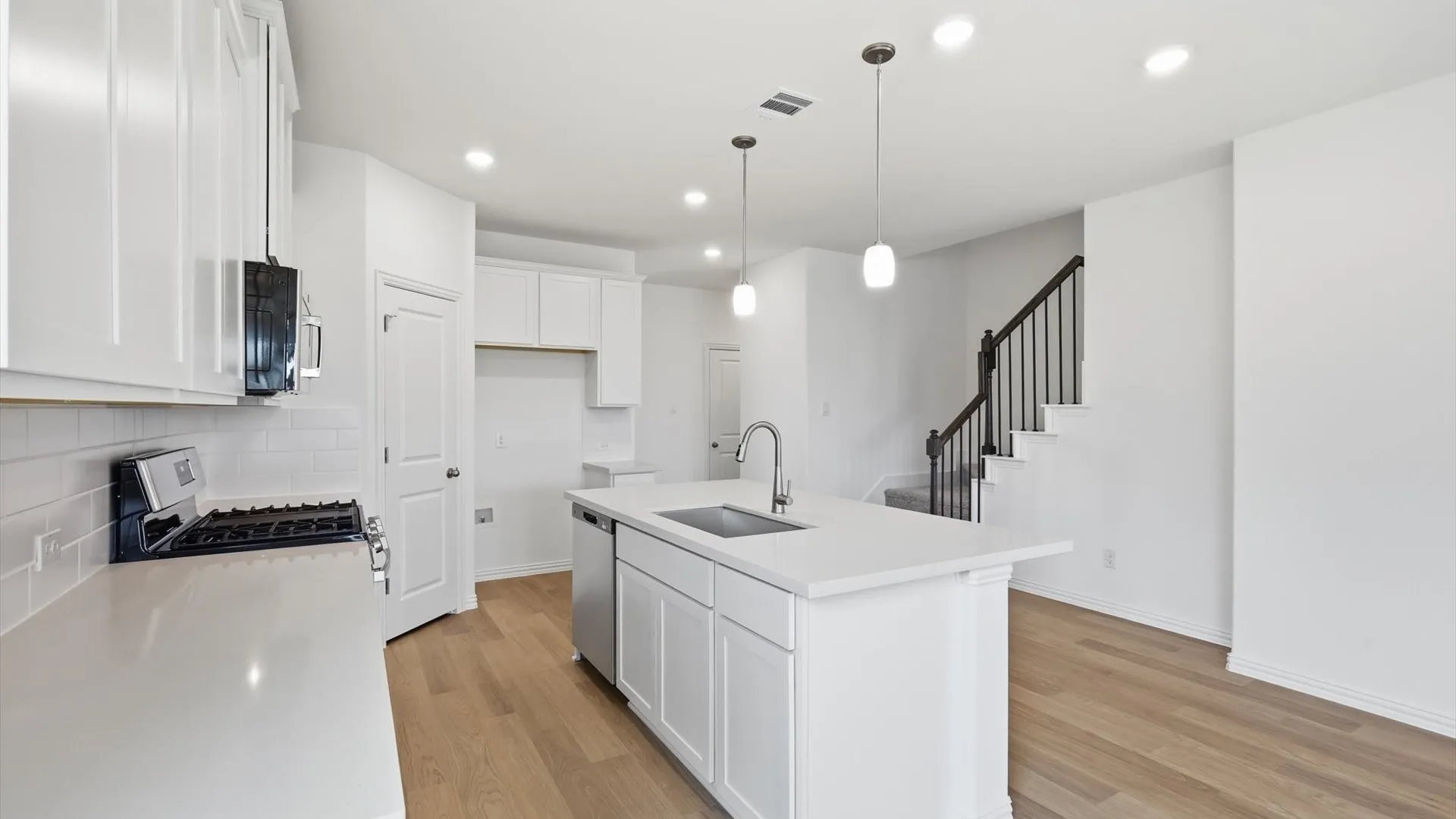 Contemporary kitchen featuring white cabinetry, light-toned countertops, a subway tile backsplash, stainless steel appliances, and wood-finish flooring