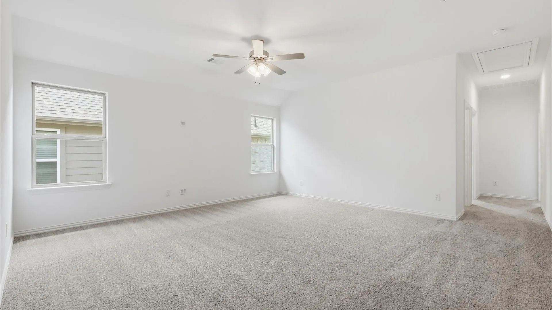 Spacious room featuring neutral carpeting, white walls, two windows, and a ceiling fan with integrated lighting