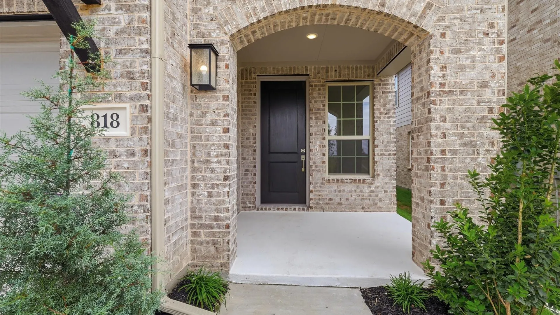 Brick facade with an arched entry porch, featuring a black front door, a window with grid detailing, and an exterior lantern sconce