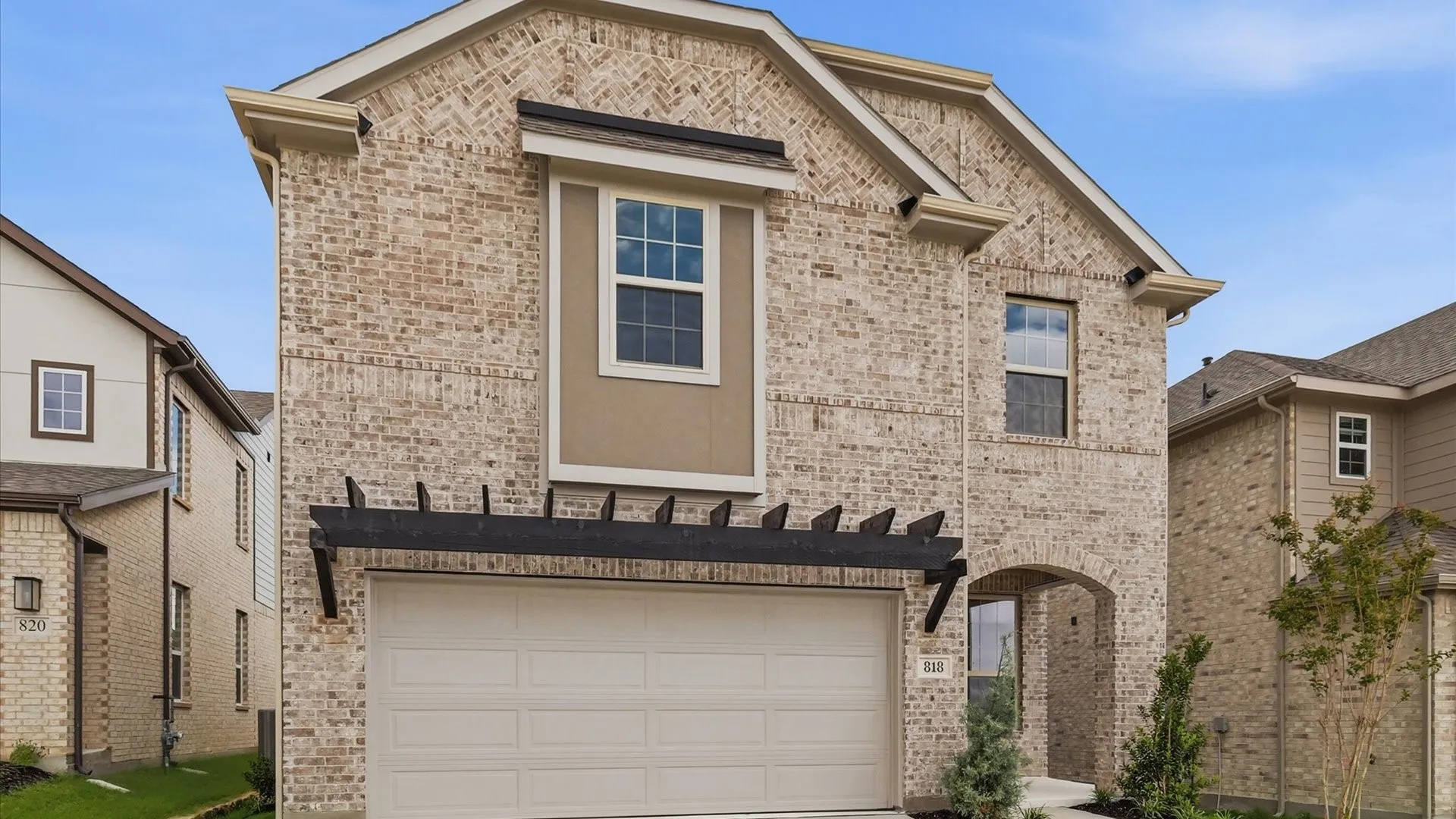 Light brick facade with a two-car garage, an arched entry, and decorative pergola detail
