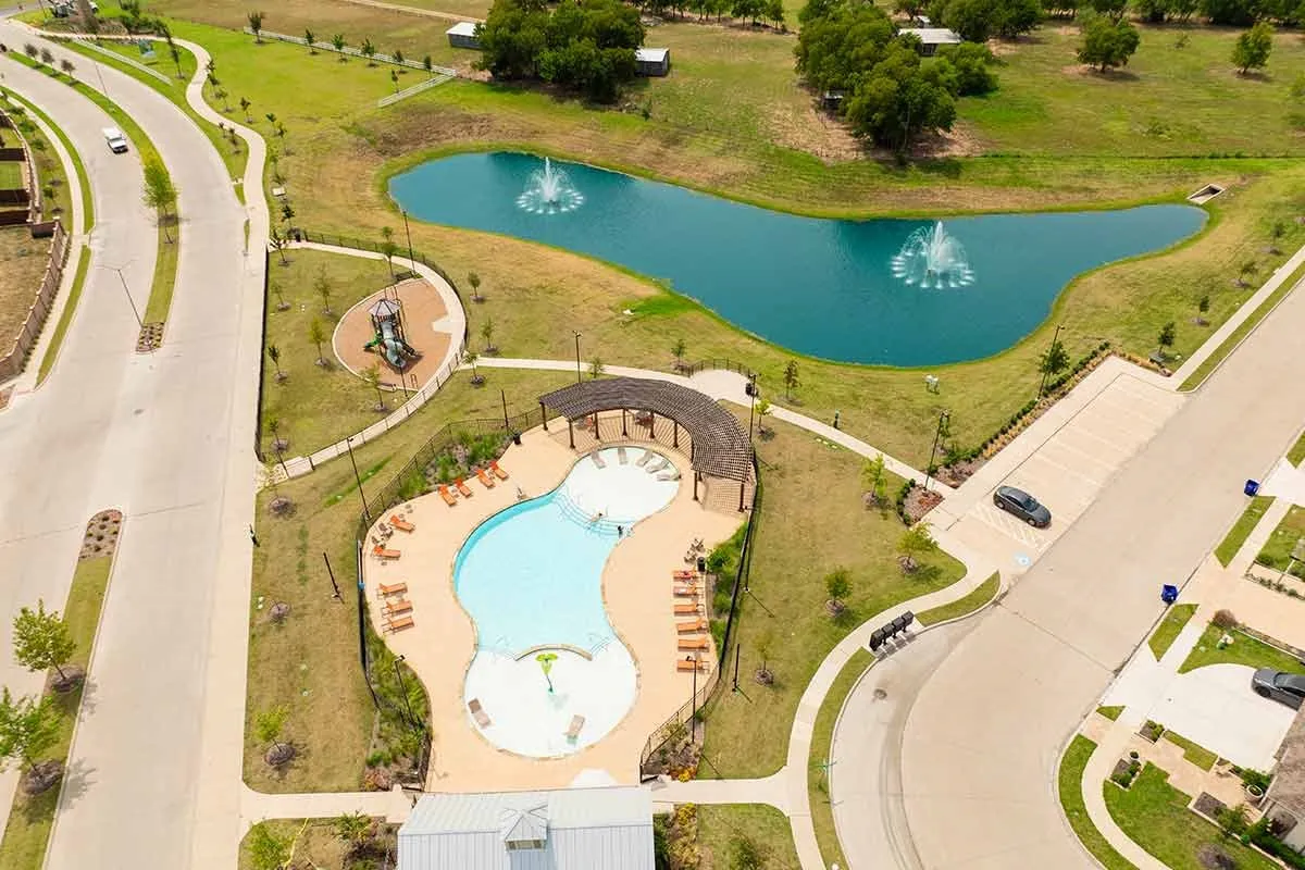 Community amenities featuring a swimming pool, shaded pool deck, playground area, and a pond with fountains