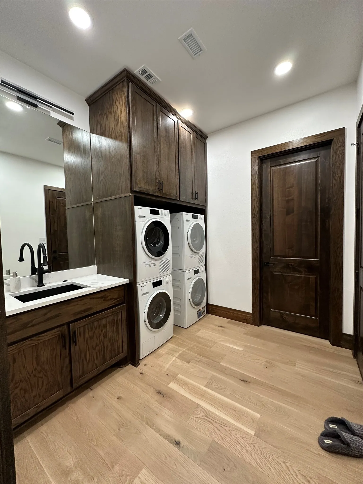 Laundry room featuring light wood finished floors, cabinet space, estacked washer and dryer, and recessed lighting