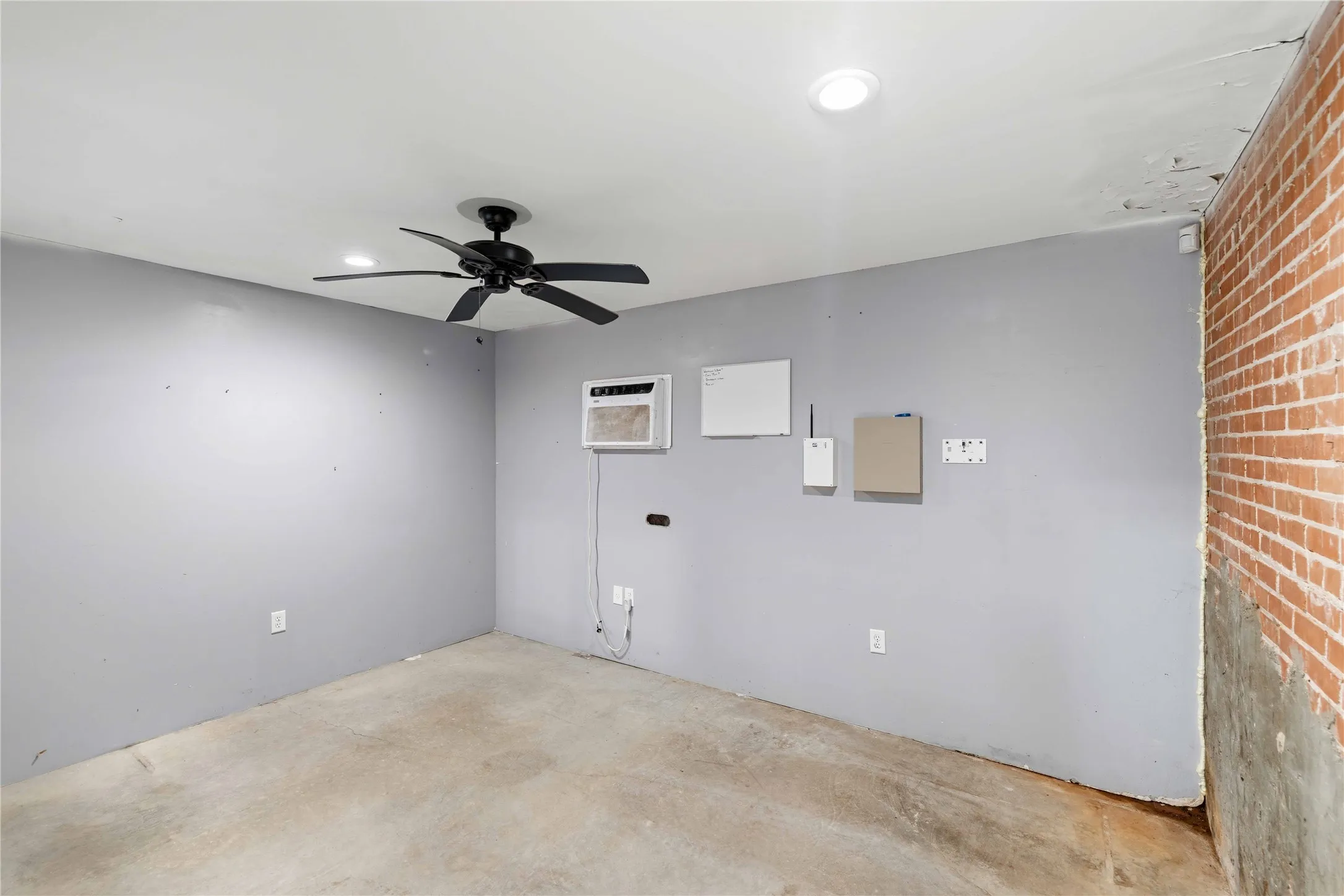 The room features a ceiling fan, a window air conditioning unit, and a concrete floor