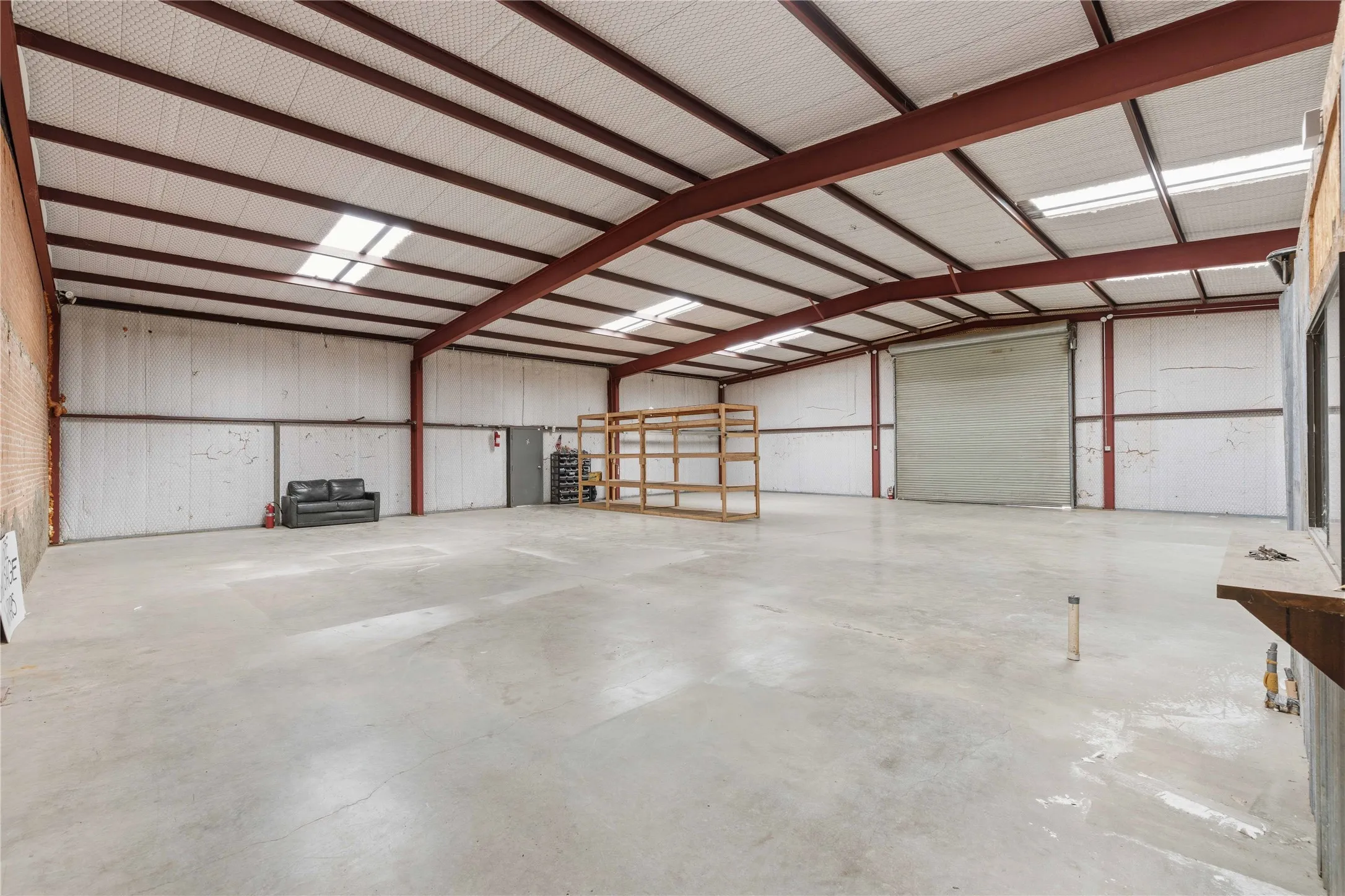 Spacious interior featuring a concrete floor, exposed metal beam ceiling, and a large roll-up door