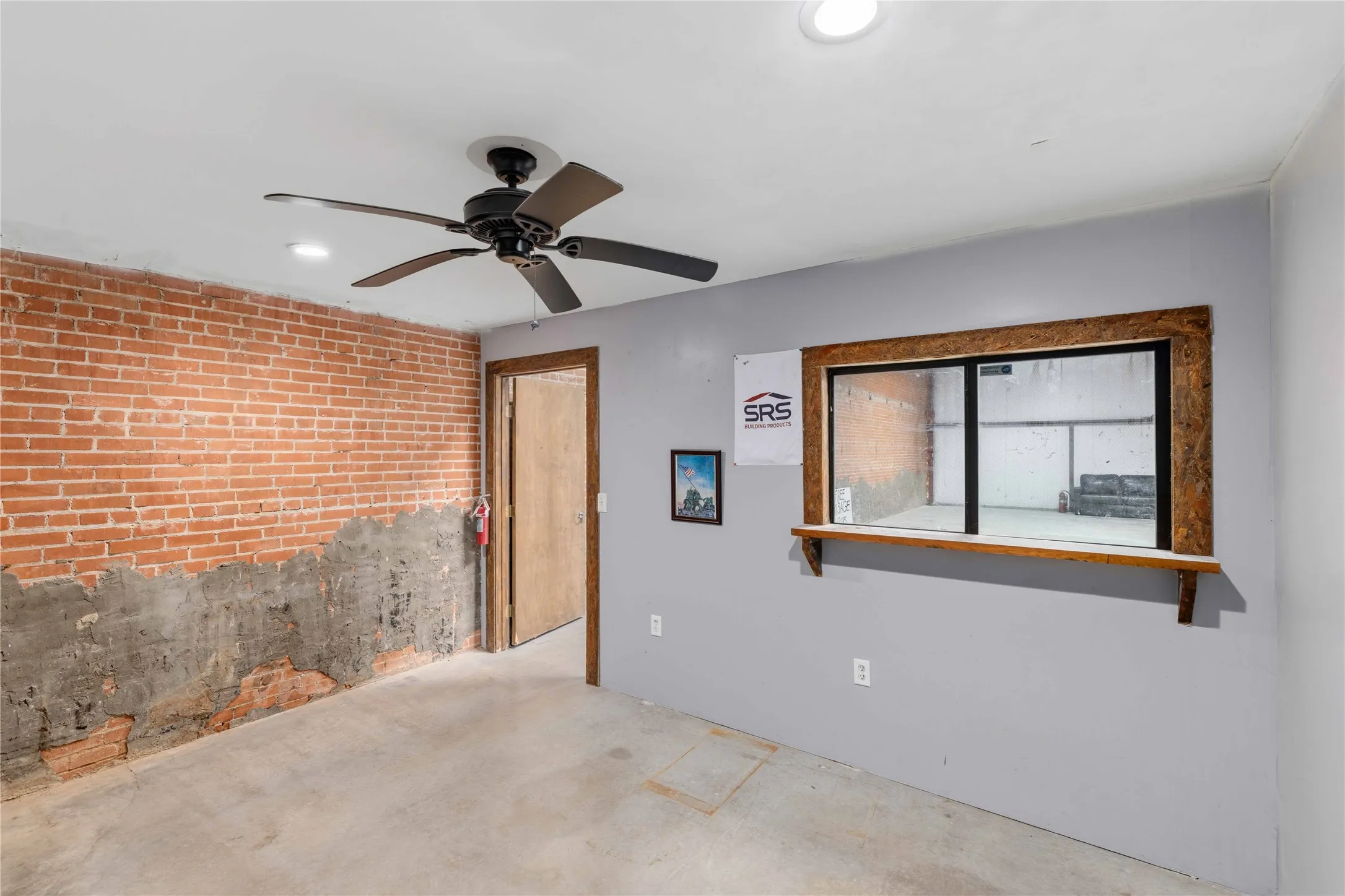 This space features an exposed brick wall, a ceiling fan, and a pass-through window with a wooden frame and shelf