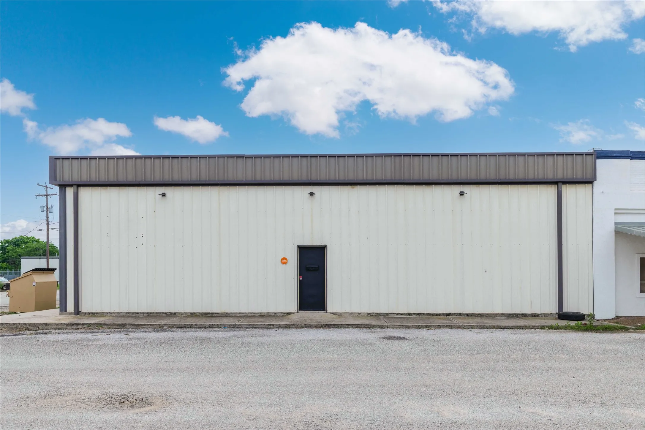 Commercial property featuring a white metal facade with a dark gray trim, a dark entry door, and an asphalt parking area